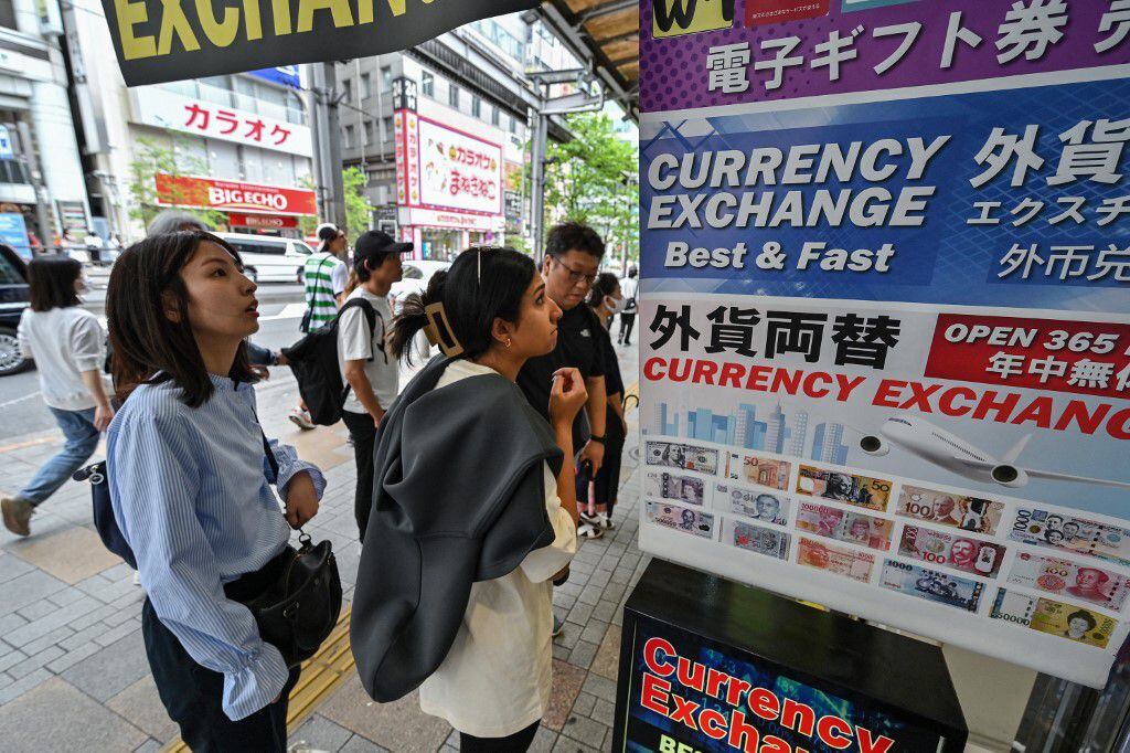 La gente se encuentra afuera de una casa de cambio, mirando el precio del yen japonés frente a monedas extranjeras, a lo largo de una calle en el centro de Tokio. Fotografía: