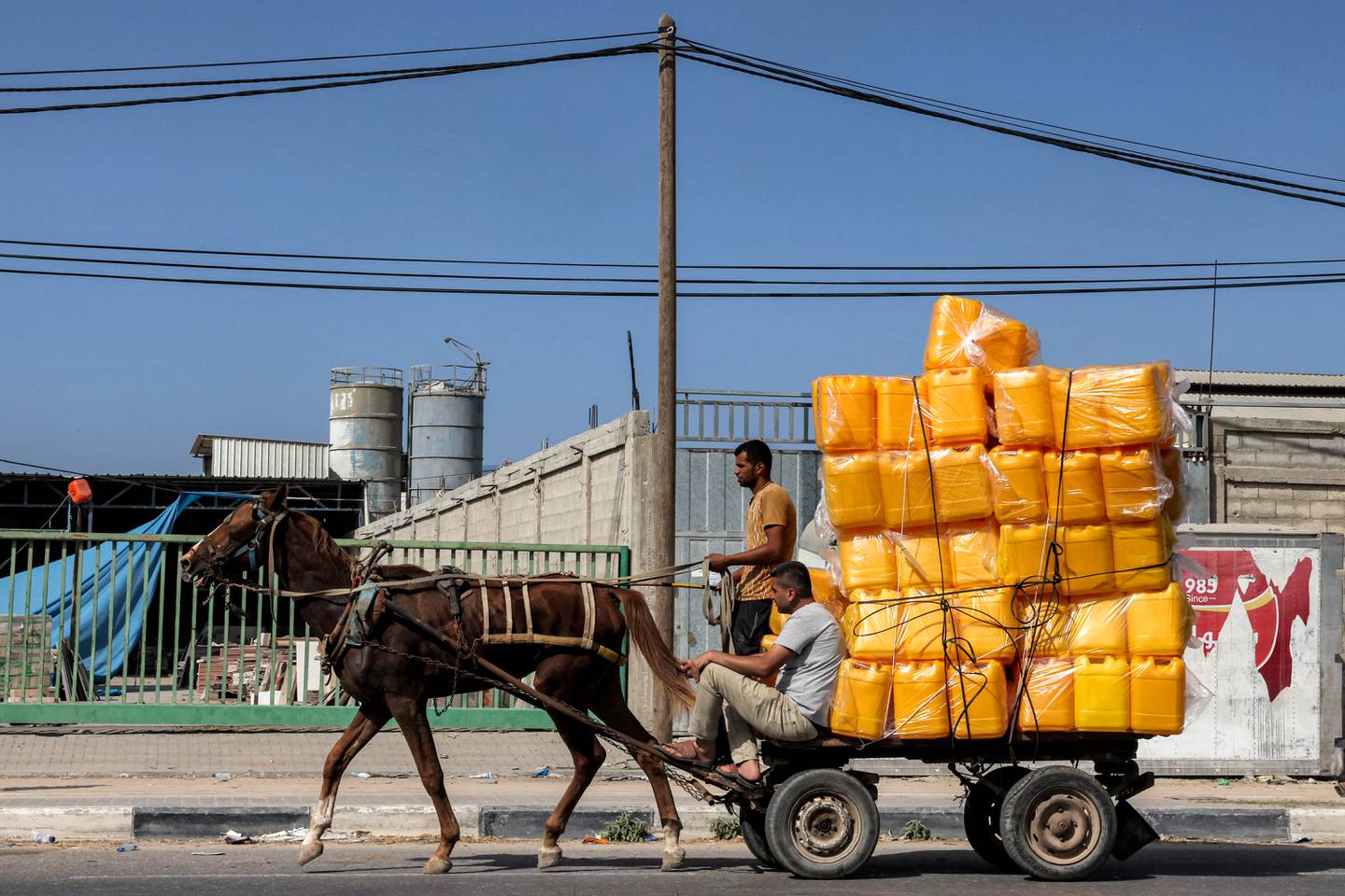 La gente viaja en un carro tirado por caballos que transporta un cargamento de bidones vacíos a lo largo de una carretera en el centro de la Franja de Gaza