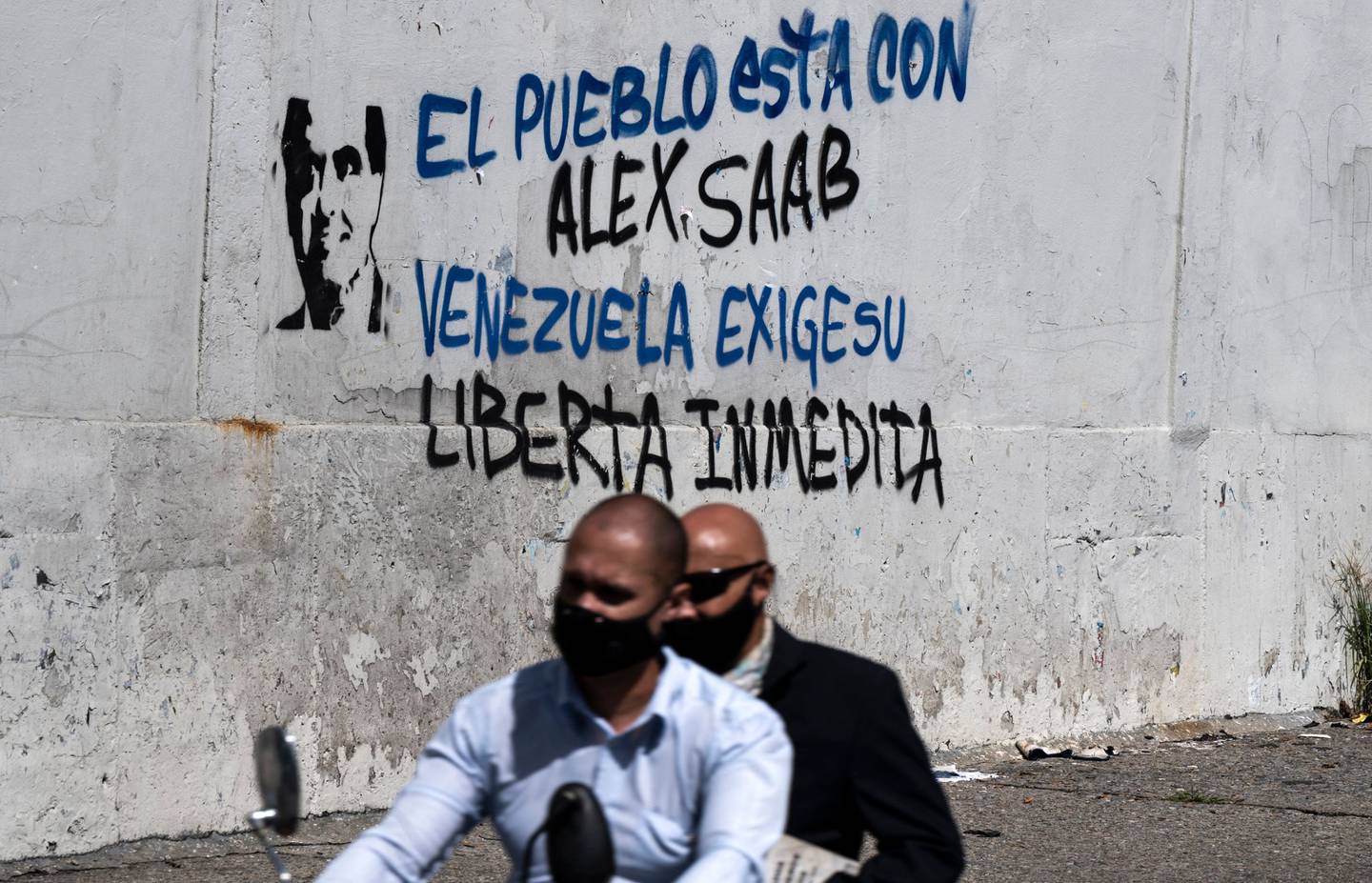 Dos hombres pasan en una motocicleta junto a un graffiti que dice "El pueblo está con Alex Saab... Venezuela exige su liberación inmediata". El nacido en Colombia es considerado un hombre clave del chavismo.