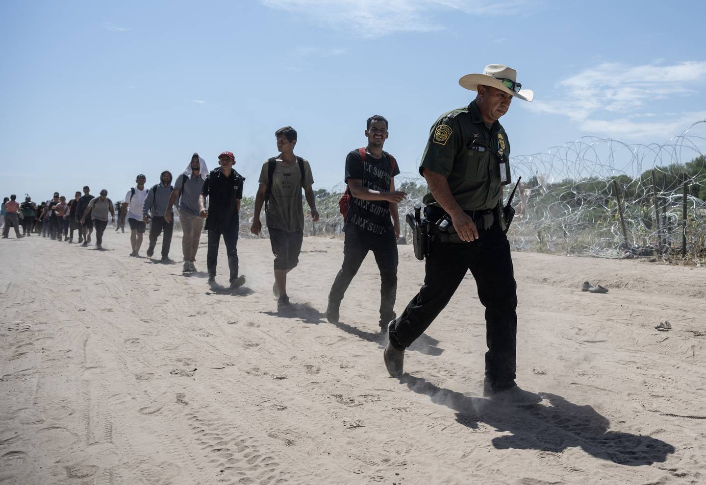Migrantes venezolanos caminan detrás de un agente de la Patrulla Fronteriza estadounidense hacia un área de procesamiento después de cruzar el Río Grande en Eagle Pass