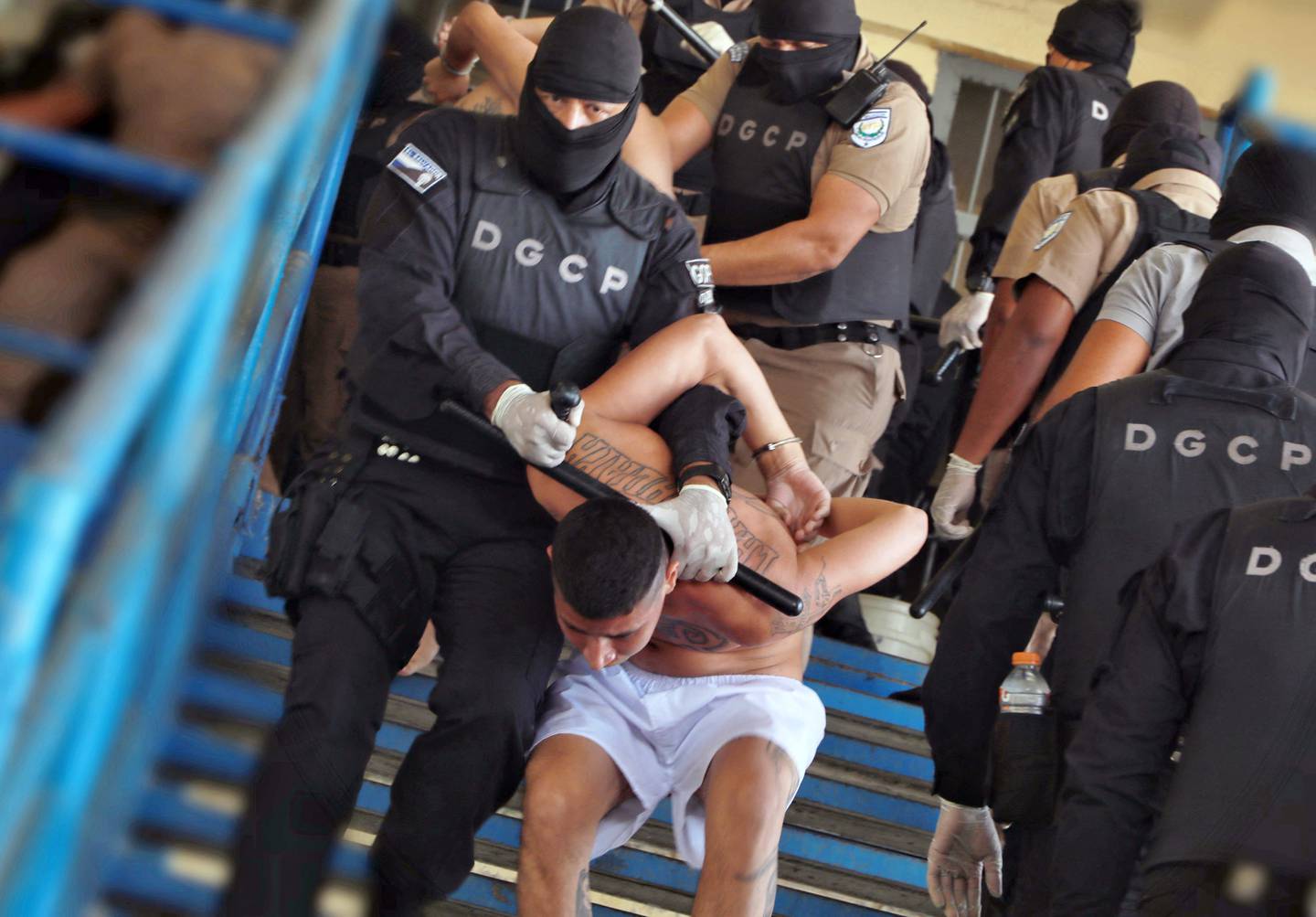 La imagen muestra a miembros de las pandillas Mara Salvatrucha y Barrio 18 cuando son trasladados por fuerzas de seguridad a un patio de la prisión en Ciudad Barrios, El Salvador.