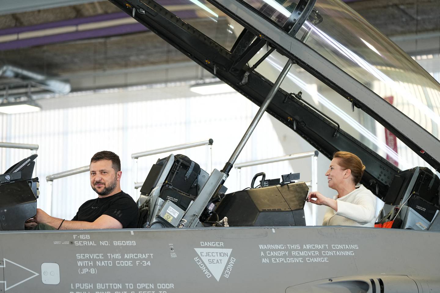 El presidente de Ucrania, Volodymyr Zelensky (izq.), y la primera ministra danesa, Mette Frederiksen (der.), reaccionan sentados en un avión de combate F-16 en el hangar de la base aérea de Skrydstrup en Vojens, al norte de Dinamarca.