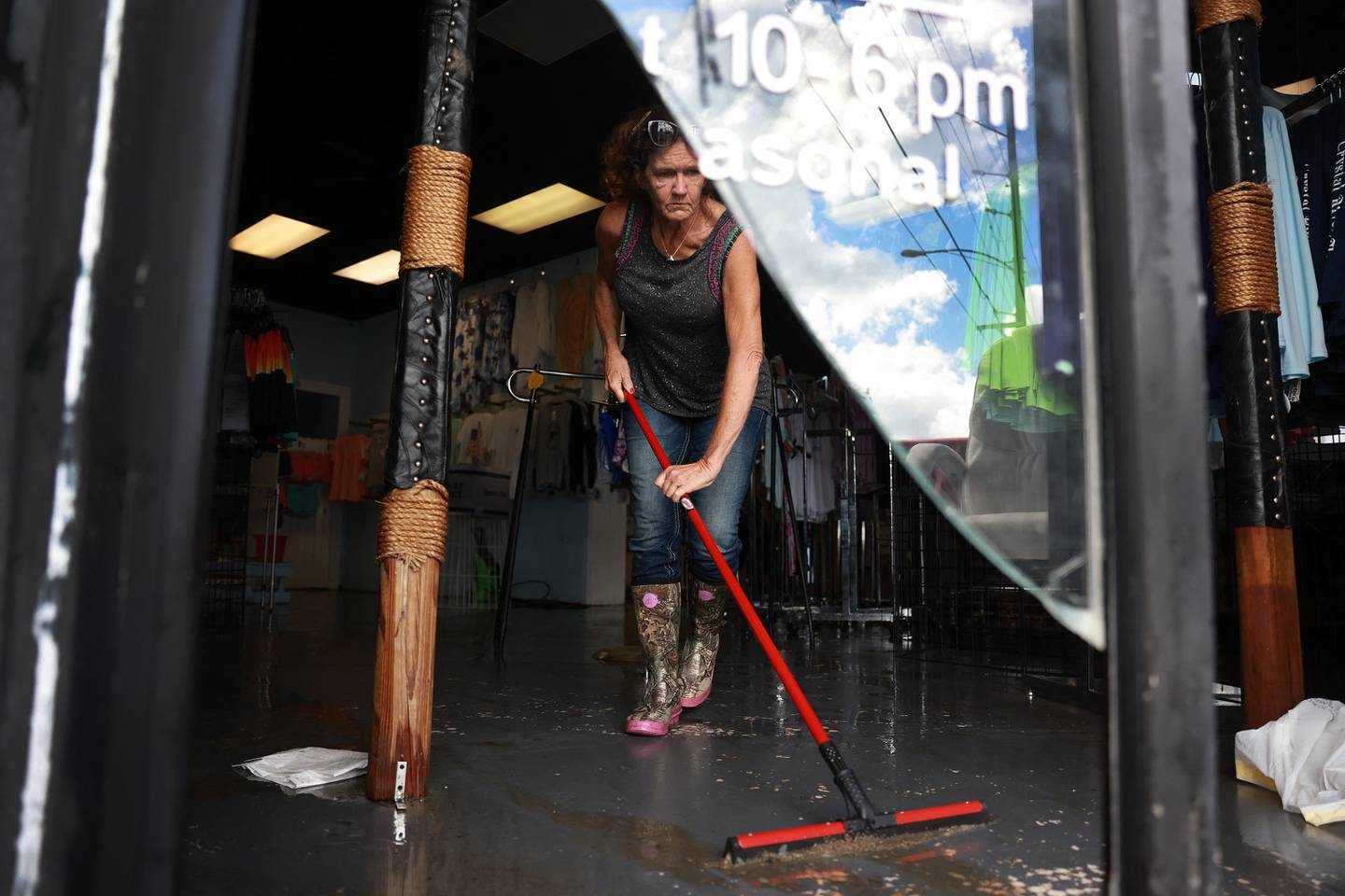 Tracy Helm usa una escobilla de goma para sacar el agua de Salty Girls Beach Shop después de que las aguas la inundaron cuando el huracán Idalia pasó frente a la costa