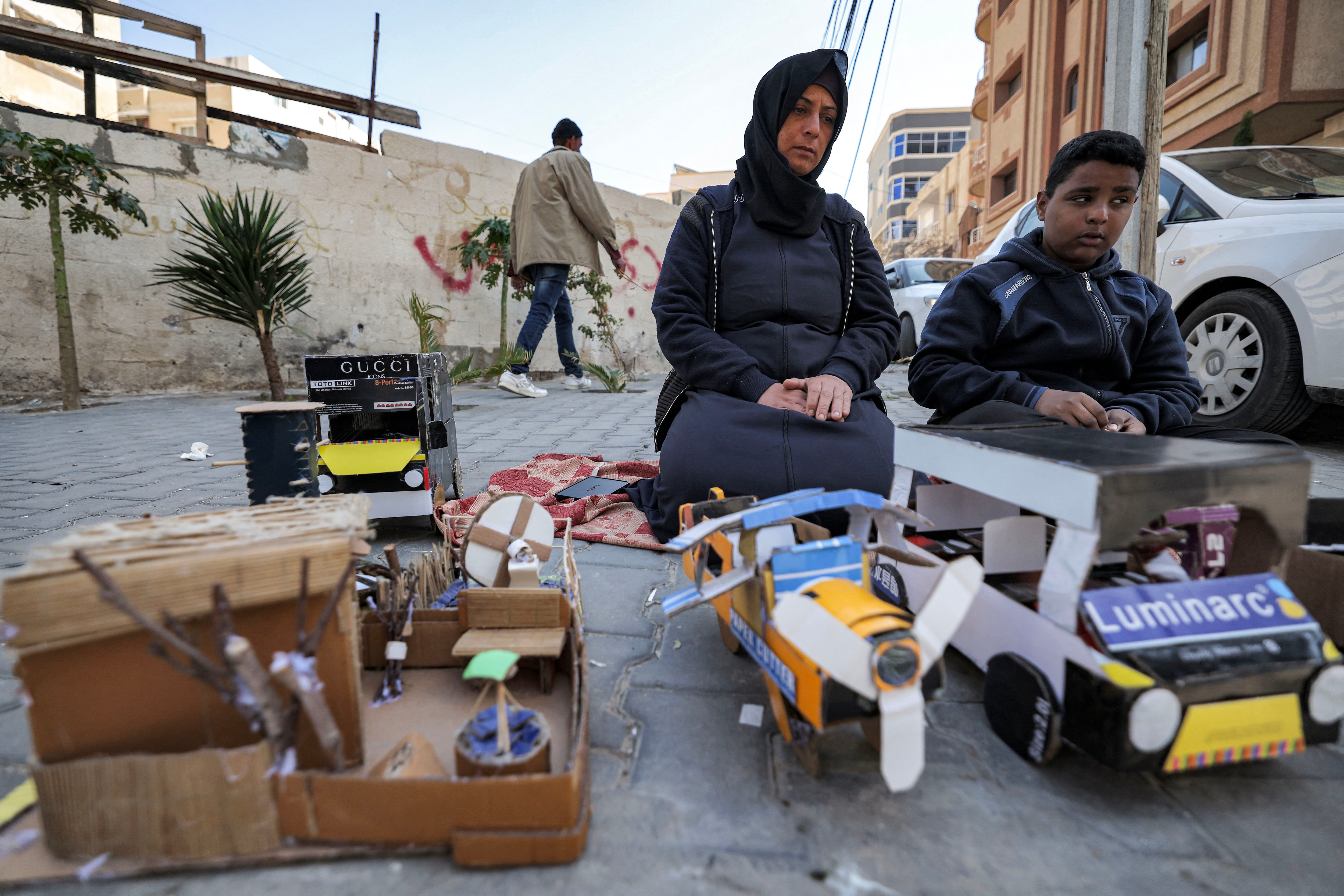 Islam Abu Taima (izquierda), una mujer palestina de 39 años, se sienta con su hijo mientras venden figuras de cartón que fabricaron para usar como juguetes para niños en el campamento de al-Shati para Refugiados palestinos en la Franja de Gaza.