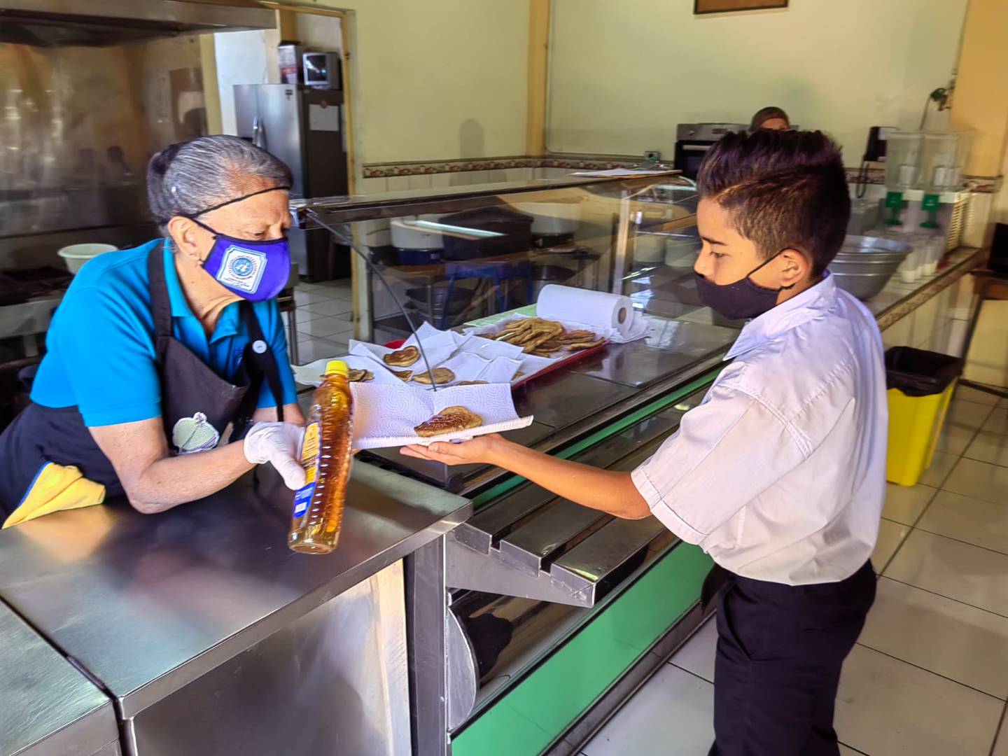 El lunes 22 de febrero del 2022, en la Escuela Naciones Unidas del barrio del mismo nombre en San José, el comedor escolar funcionaba puras tejas para una población de 468 estudiantes. En la foto, el estudiante Sebastián Segura Galán recibe su desayuno de manos de doña Rita María Pérez Garbanzo, cocinera.