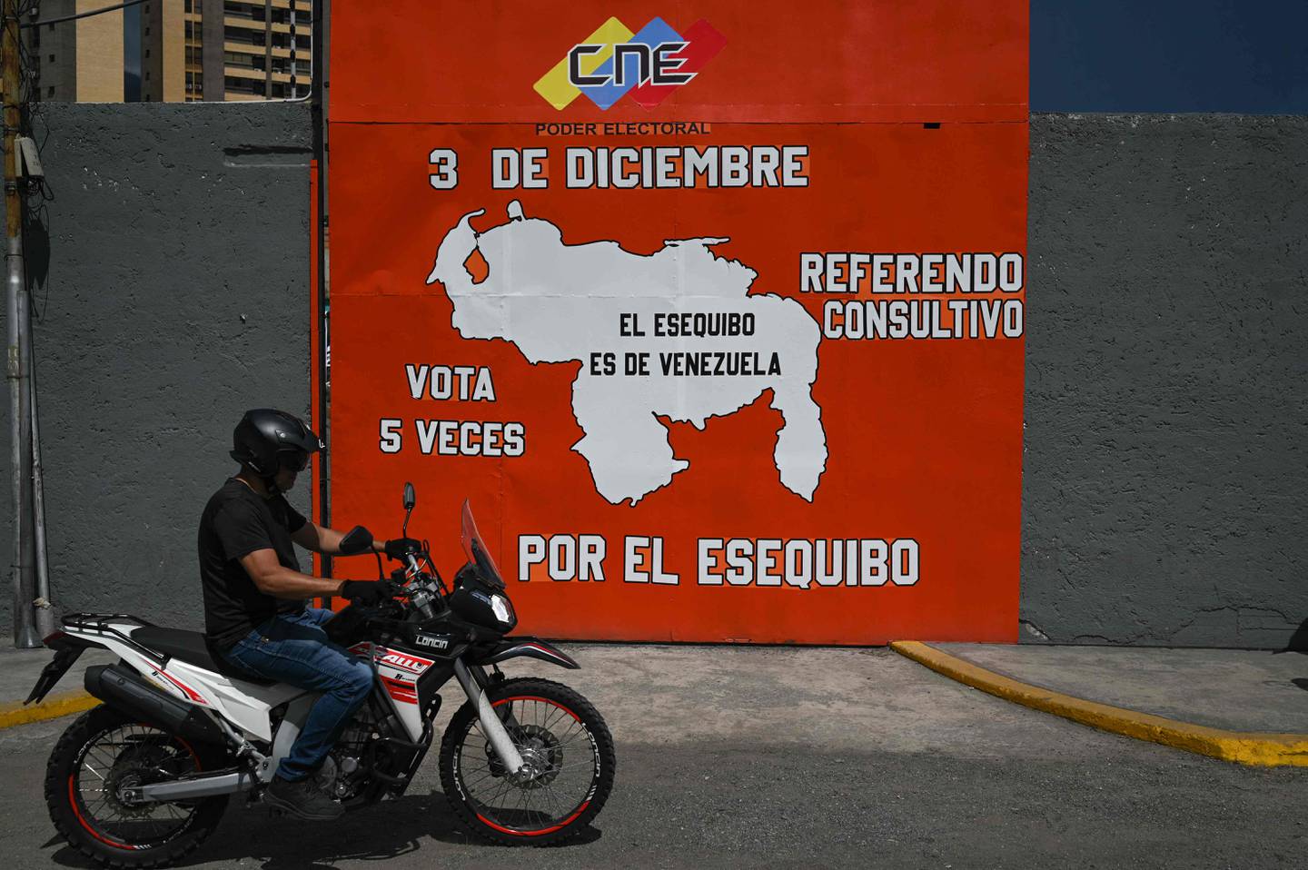 Un hombre en motocicleta pasa junto a un mural que hace campaña a favor de un referéndum para pedir a los venezolanos que consideren la anexión de la región de Esequibo administrada por Guyana, en el barrio 23 de Enero de Caracas.