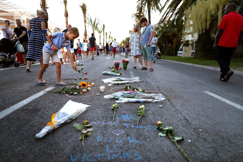 Un niño pone flores junto a rastros de sangre en el 'Promenade des Anglais', donde el camión se estrelló contra la multitud durante las celebraciones del Día de la Bastilla, en Niza, Francia, el 16 de julio de 2016. (EFE/EPA/IAN LANGSDON)