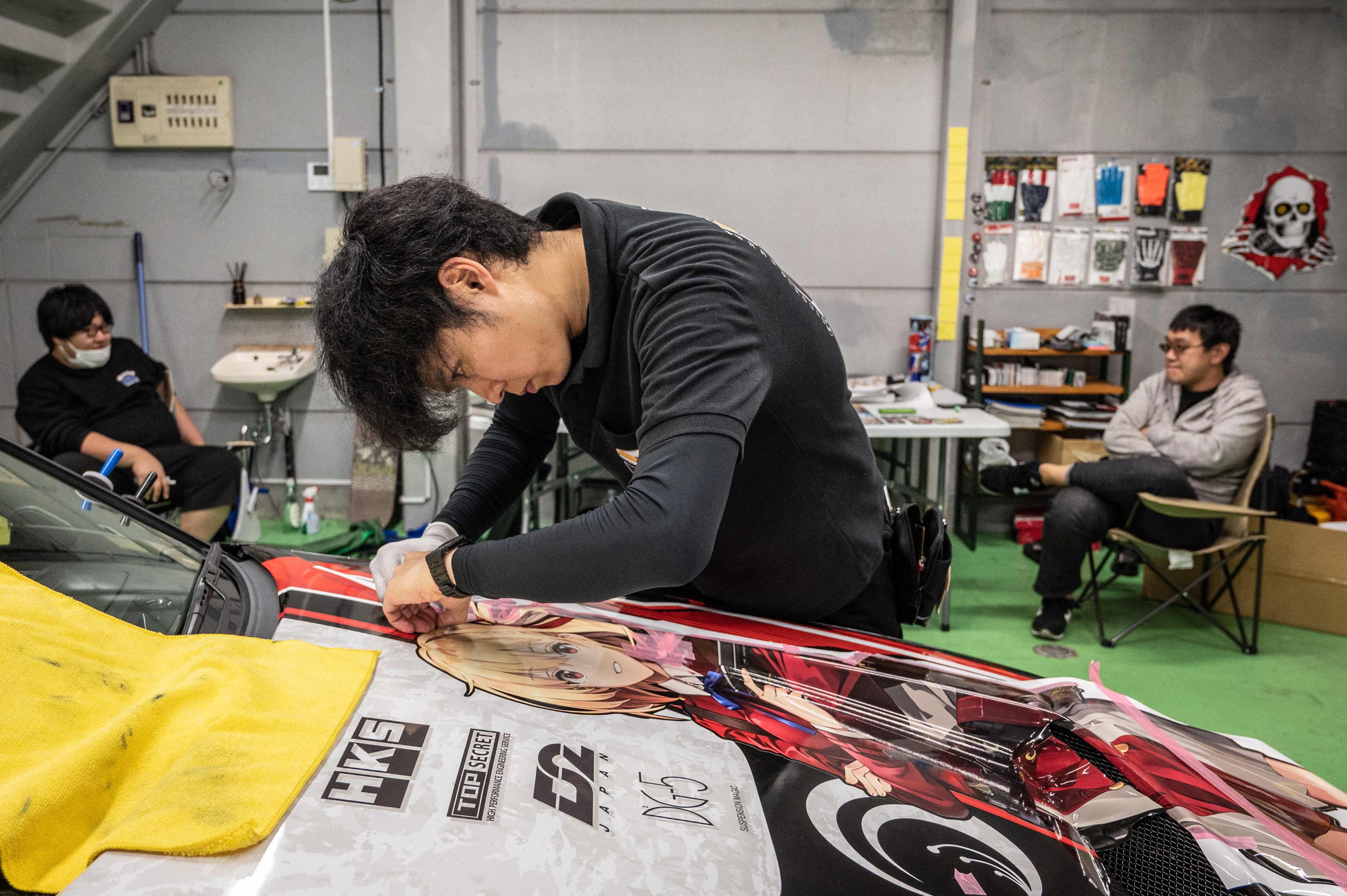 El especialista en rotulación de automóviles, Shin Kudo, aplica una envoltura de vinilo con un personaje de anime a un Nissan Skyline en un taller en Sugito, Saitama, Japón. Fotografía: