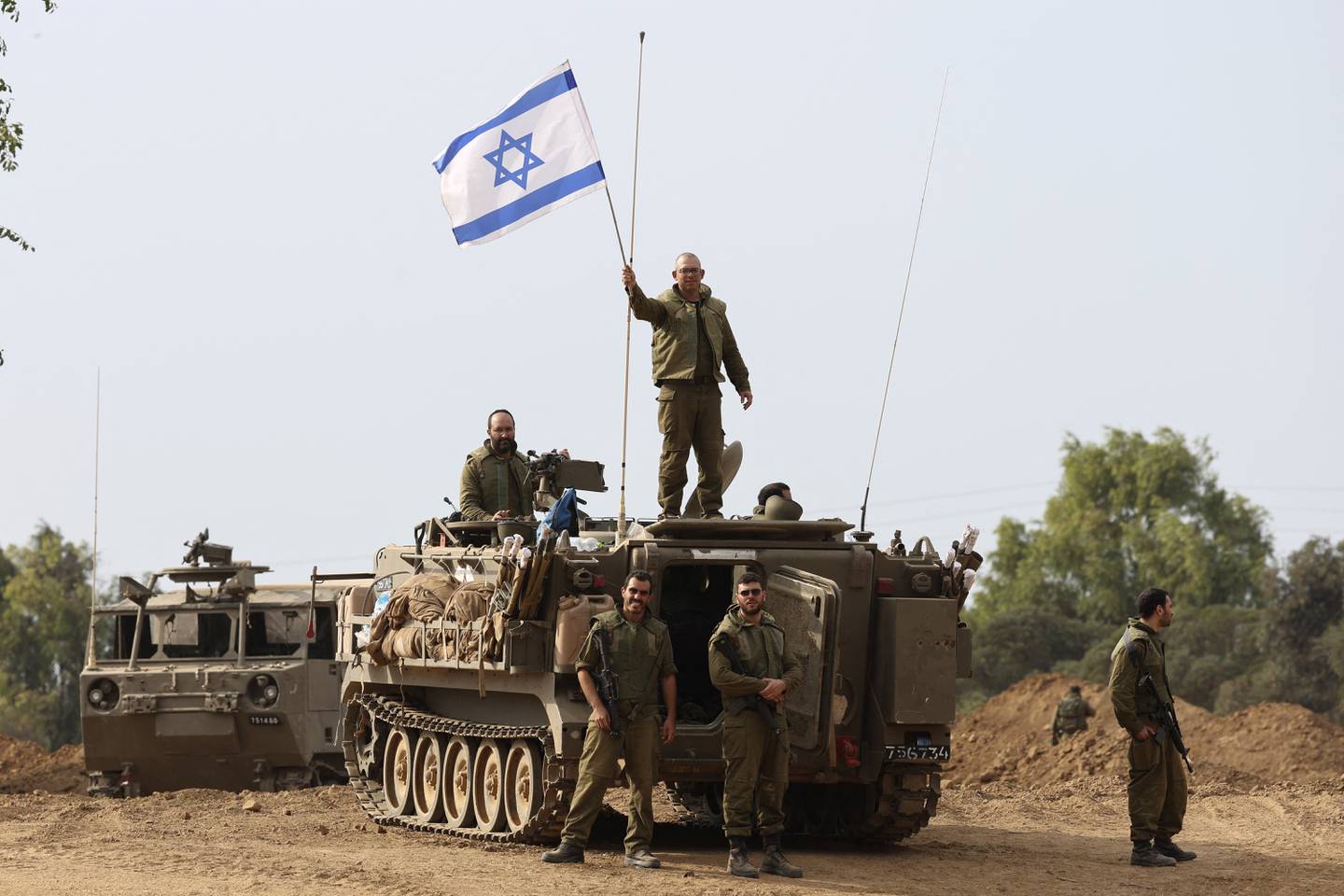 Soldados israelíes ondean su bandera nacional mientras toman posiciones en sus vehículos blindados cerca de la frontera con Gaza