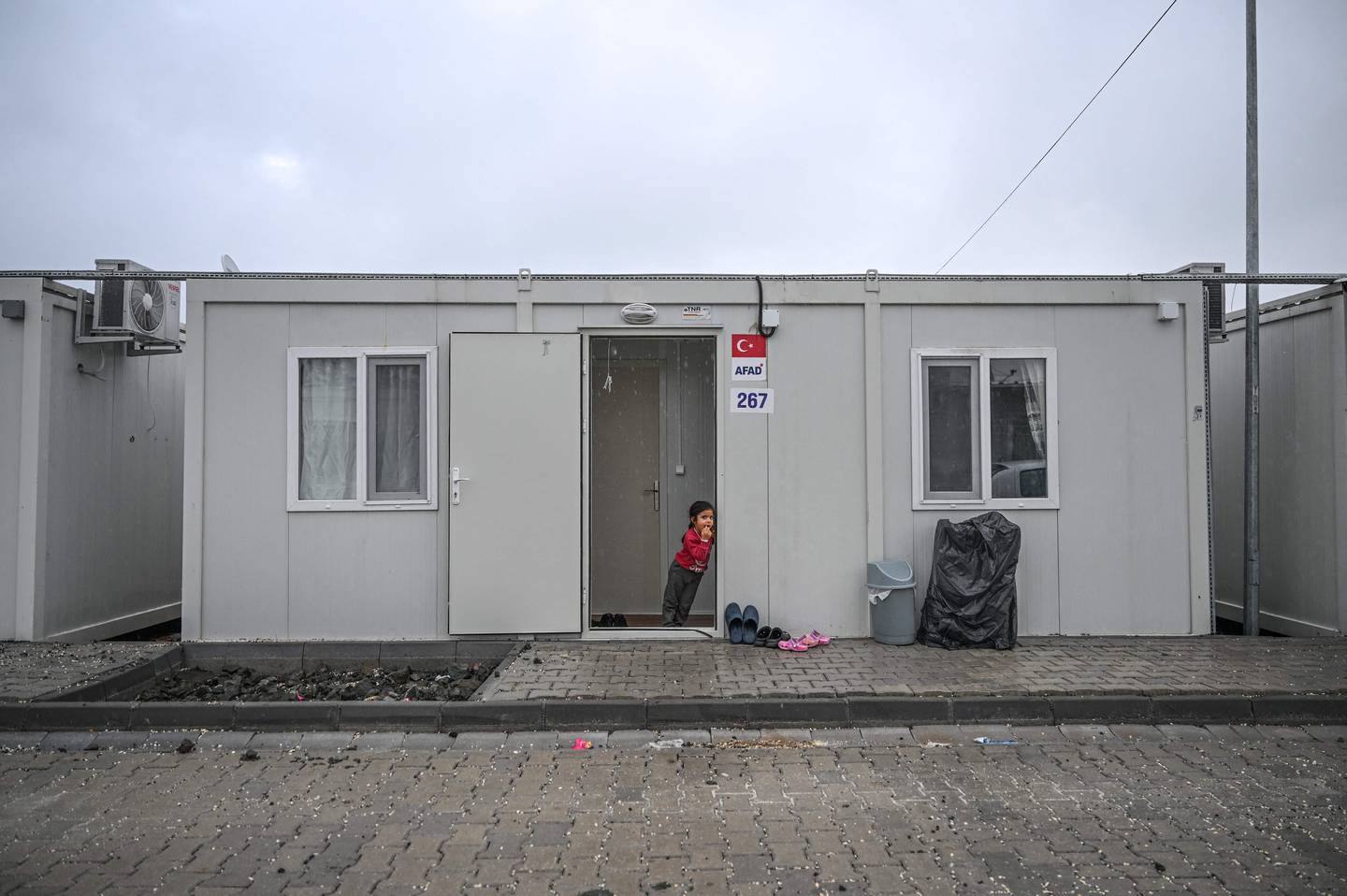 Un niño se encuentra en la puerta de una casa estilo contenedor, que alberga a las víctimas del terremoto de febrero de 2023, en Antakya, provincia de Hatay.