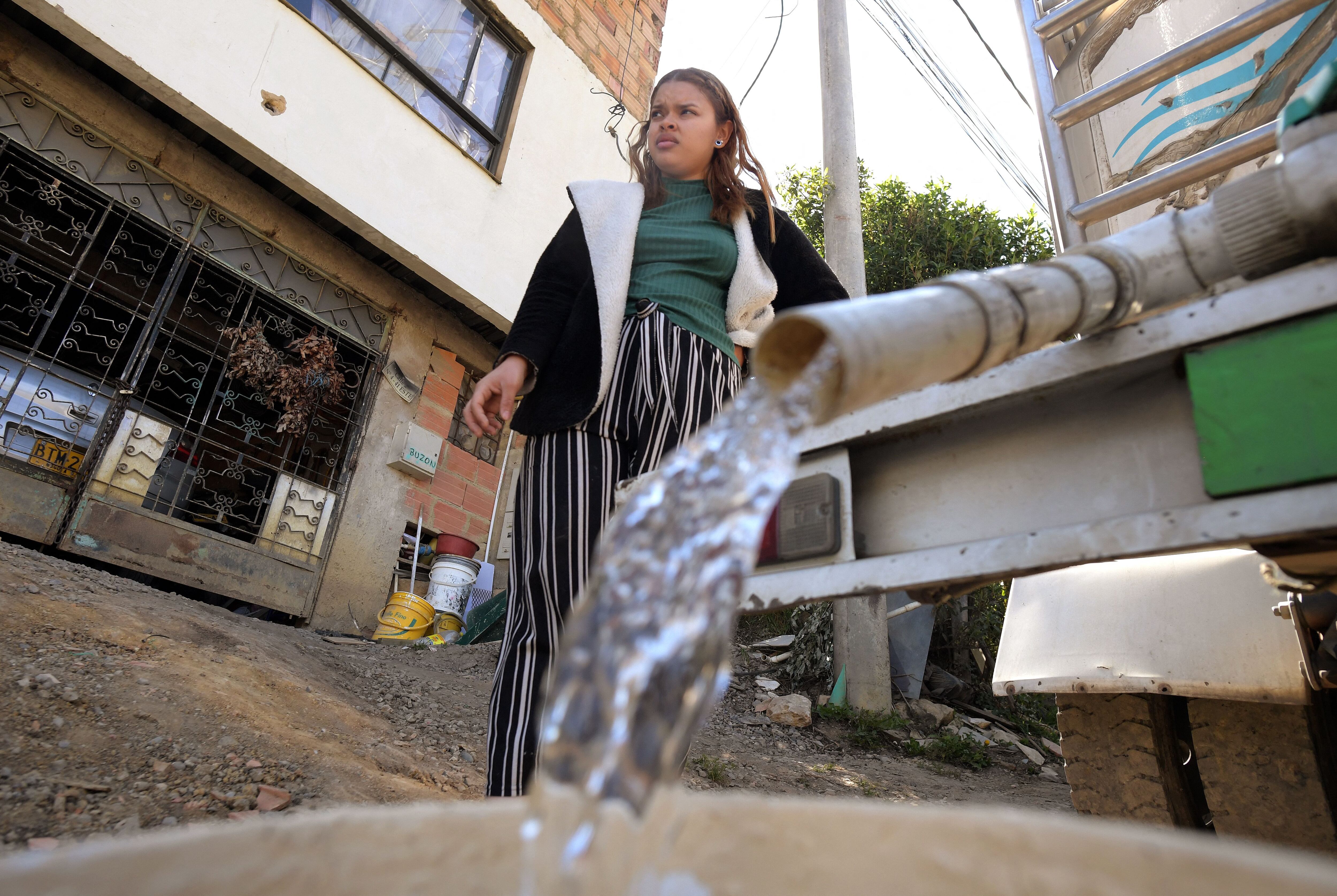 A woman collects drinking water from a water truck in La Calera, near Bogota, April 10, 2024. A tanker truck delivers water on the steep streets of La Calera, a neighbour of the Colombian capital. For weeks now, this region considered rich in water resources has been experiencing unprecedented shortages due to the El Ni�o phenomenon and climate change. (Photo by Daniel MU�OZ / AFP)