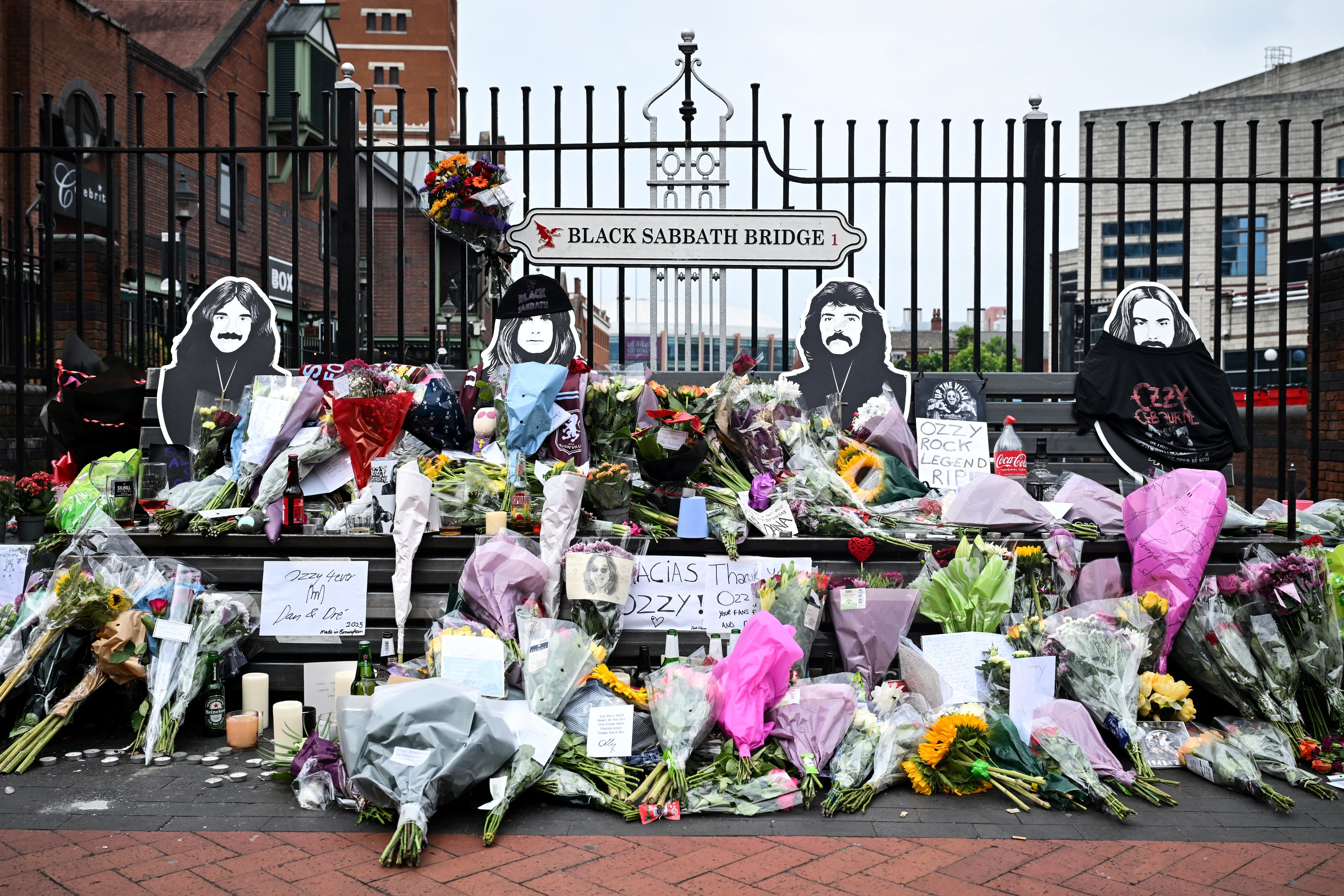 A photograph taken on July 23, 2025 shows flowers, candles and drawings left at a makeshift memorial on Black Sabbath Bridge, in tribute of late British singer-songwriter Ozzy Osbourne, in Birmingham, central England, a day after his death. Tributes poured in on July 23, 2025 for hell-raiser singer Ozzy Osbourne as tearful fans laid flowers in his hometown and his Black Sabbath band mates mourned the death of their legendary heavy metal frontman, just weeks after he played an epic farewell concert in their Birmingham hometown. Osbourne, nicknamed the "Prince of Darkness" who famously once bit off the head of a bat while on stage, died on July 22, 2025 at the age of 76, his family said. (Photo by JUSTIN TALLIS / AFP)
