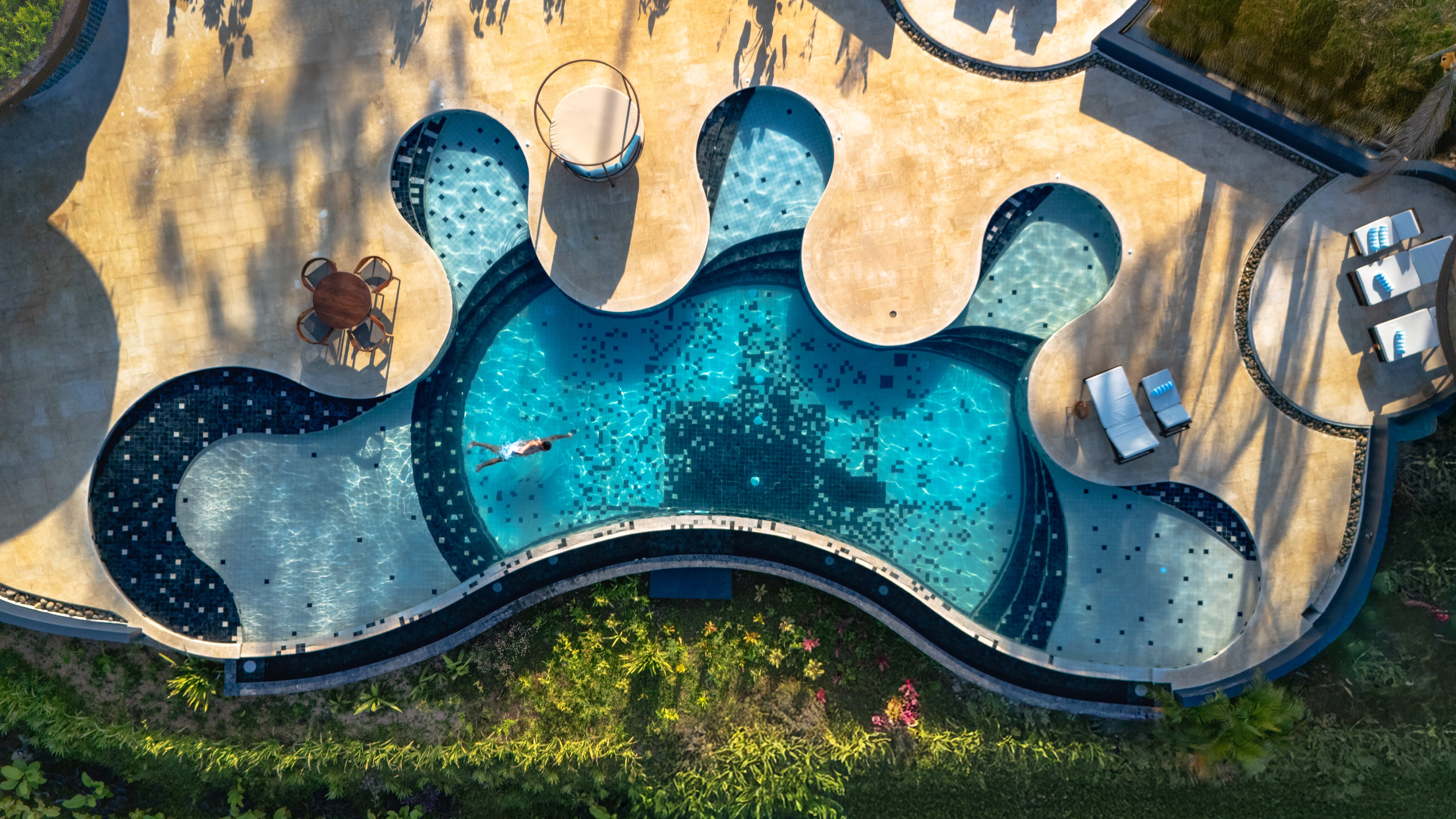 Piscina del hotel Origins Astral vista desde drone con un huésped nadando en el resort de lujo ubicado en Bijagua de Upala, Costa Rica.