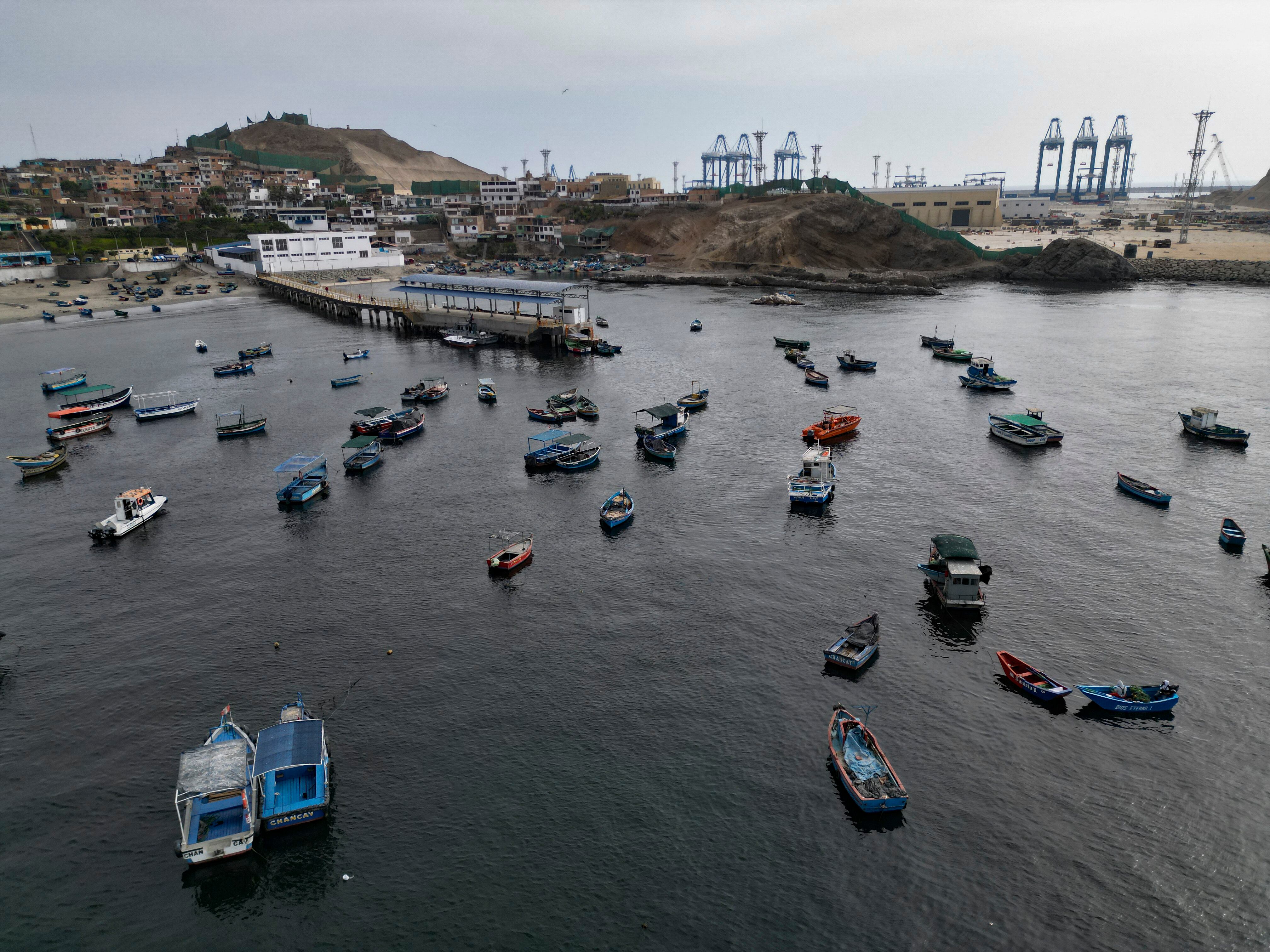 Vista aérea de embarcaciones pesqueras tradicionales ancladas en el puerto de Chancay, con las grúas del "megapuerto" al fondo, a 78 kilómetros al norte de la capital peruana, Lima. Foto por Cris BOURONCLE / AFP