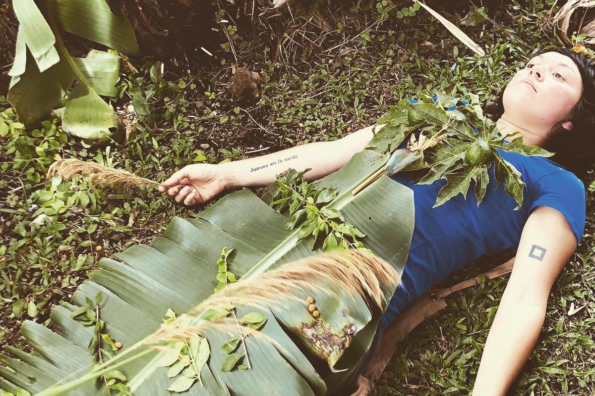 La artista visual y educadora Mariela Richmond, cubierta de hojas en una finca, gestiona el proyecto La Escuelita de la Tierra.