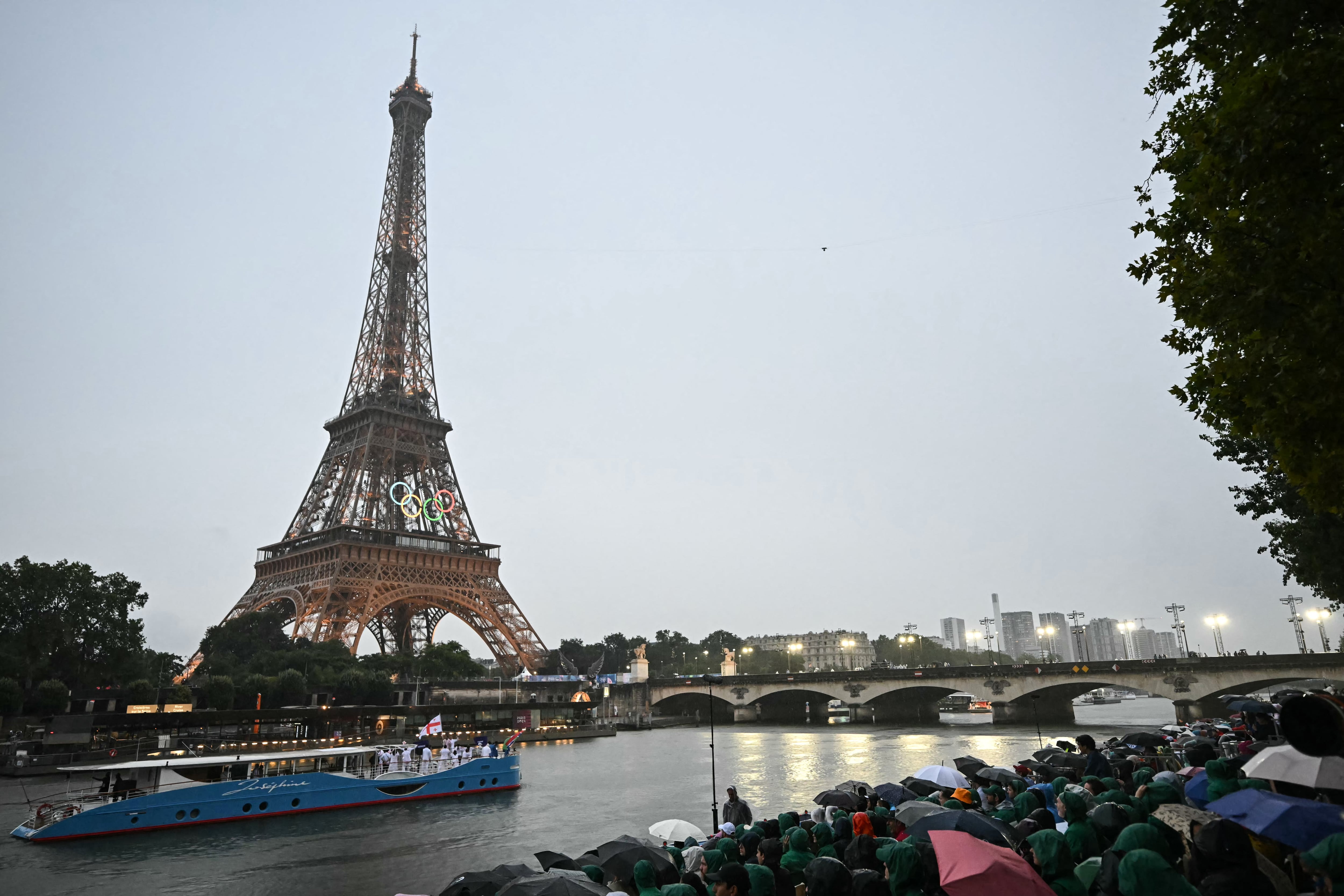 Las delegaciones de Gambia y Georgia navegan en un bote por el río Sena durante la ceremonia de apertura de los Juegos Olímpicos de París 2024 en París, el 26 de julio de 2024, con la Torre Eiffel visible al fondo.