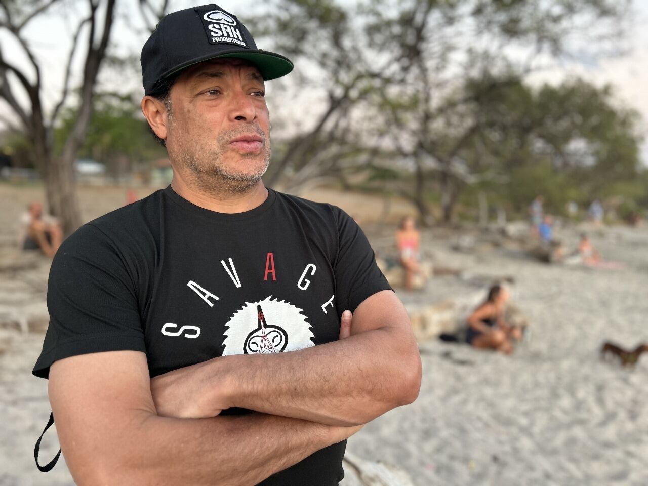Foto de Robert Trujillo en primer plano, con sus brazos cruzados, usa gorra y camiseta negra.