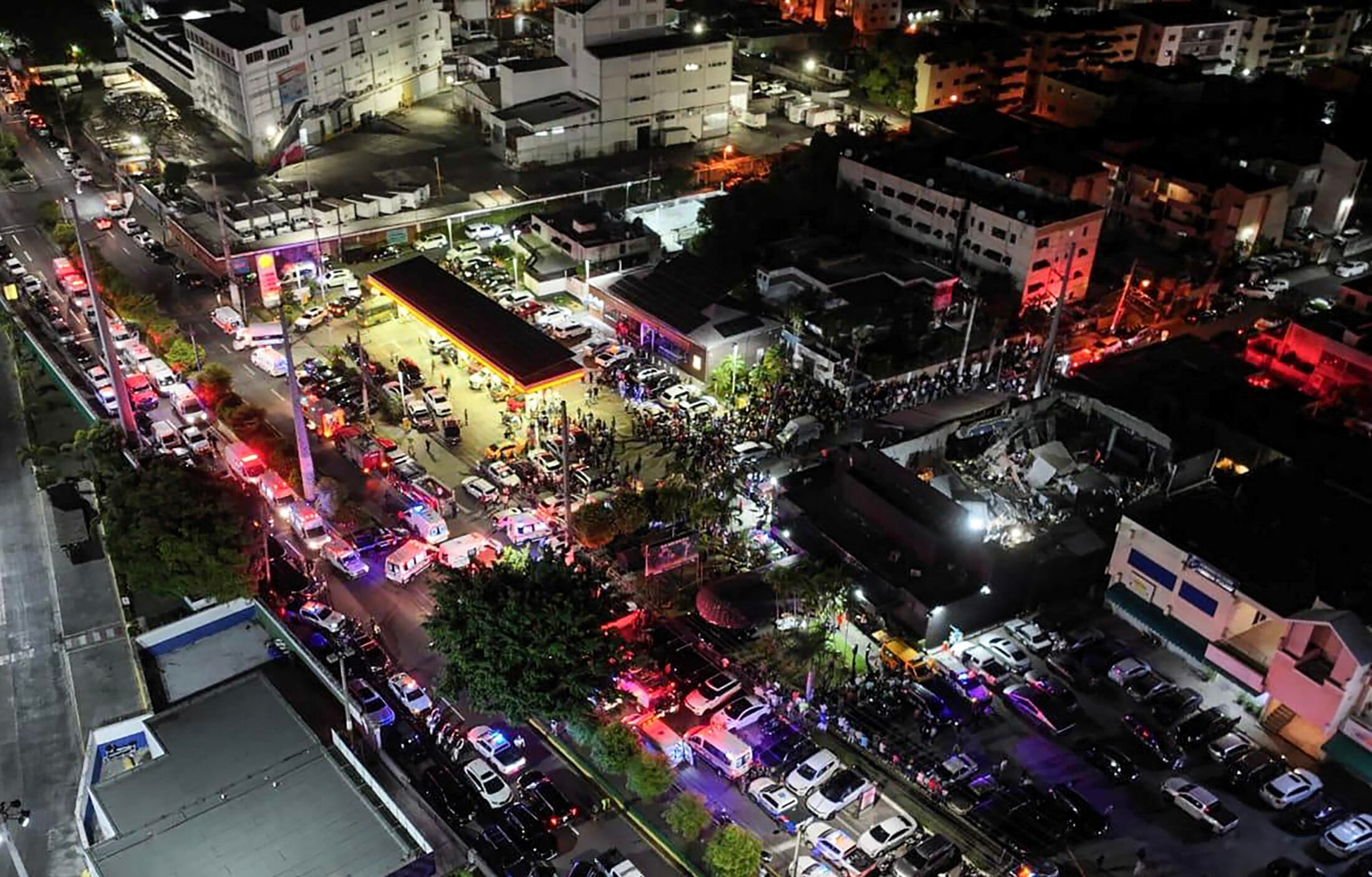 Fotografía difundida por autoridades de República Dominicana que muestra una vista aérea de personas reunidas frente a la discoteca Jet Set (der.) tras el derrumbe de su techo, en Santo Domingo, este 8 de abril. Fotografía: