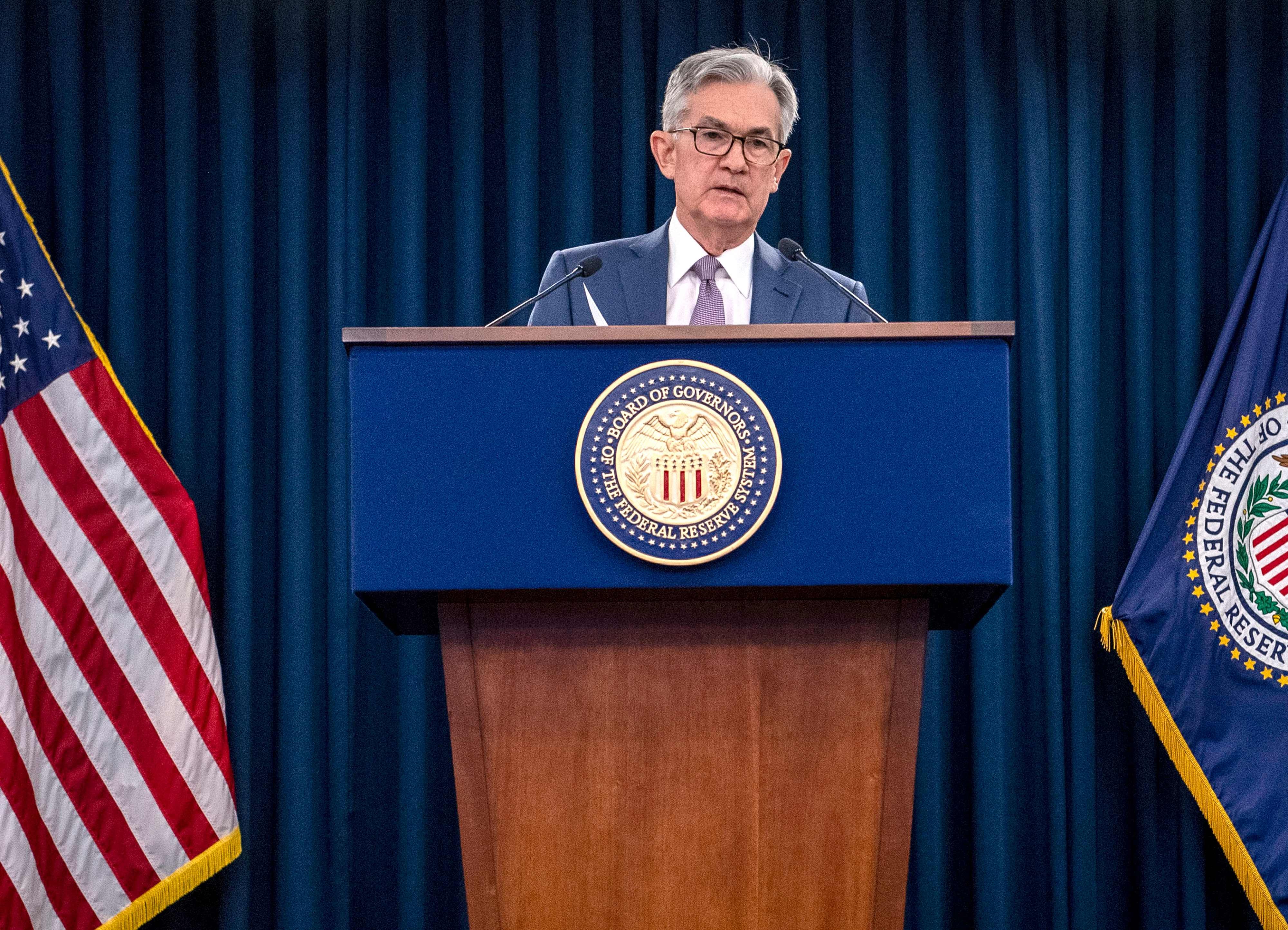 Jerome Powell, presidente de la Reserva Federal, en el podio durante una conferencia de prensa, con banderas de Estados Unidos y el emblema de la Fed al fondo.