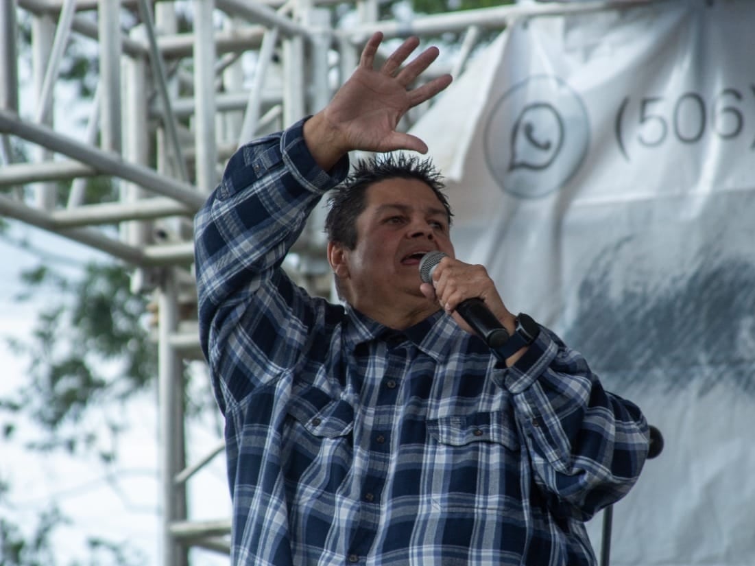 Un hombre con un micrófono en la mano izquierda y la mano derecha levantada