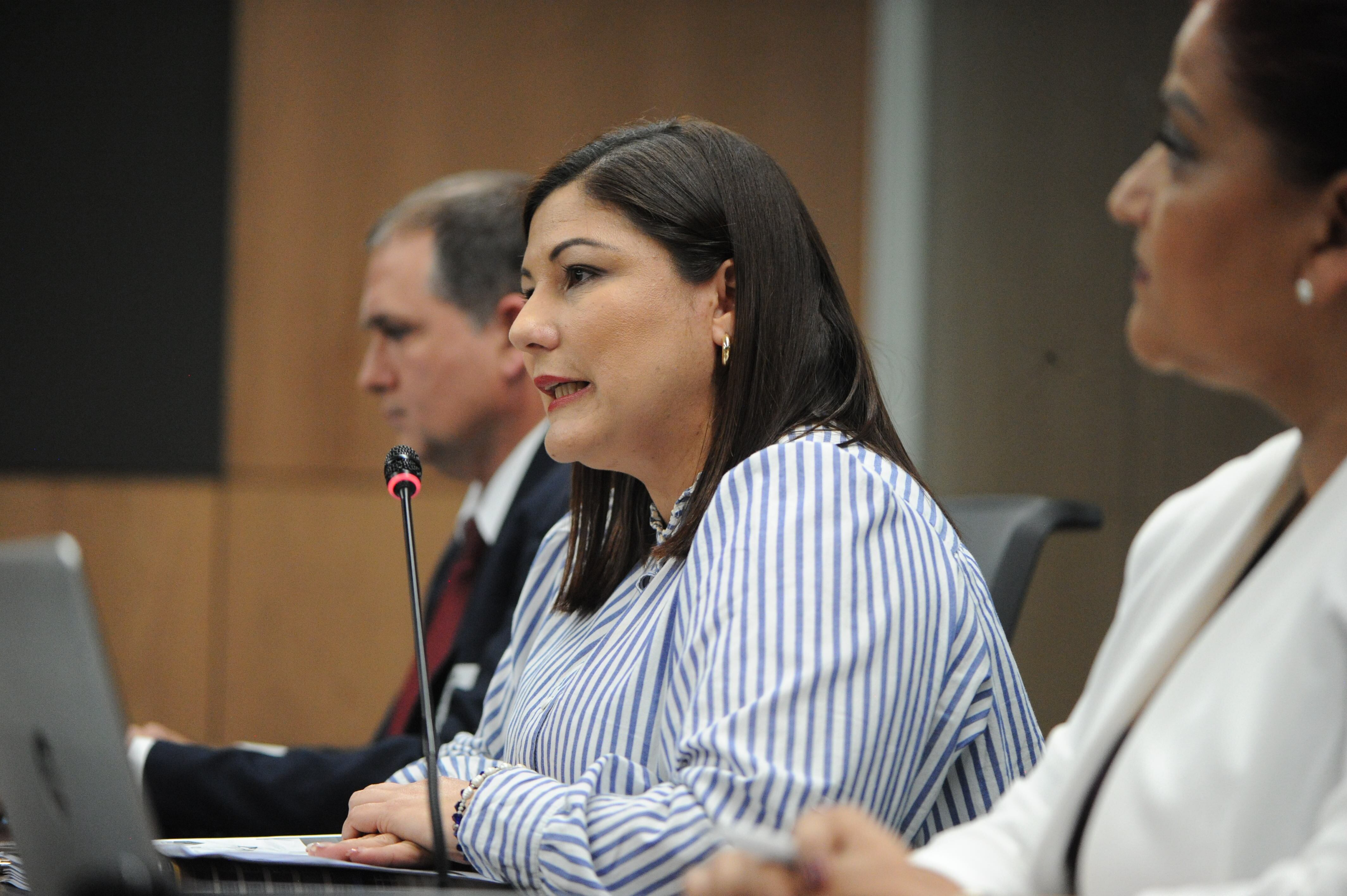 Mujer joven, blanca, gruesa, pelo a los hombros, oscuro. Da declaraciones frente a un micrófono