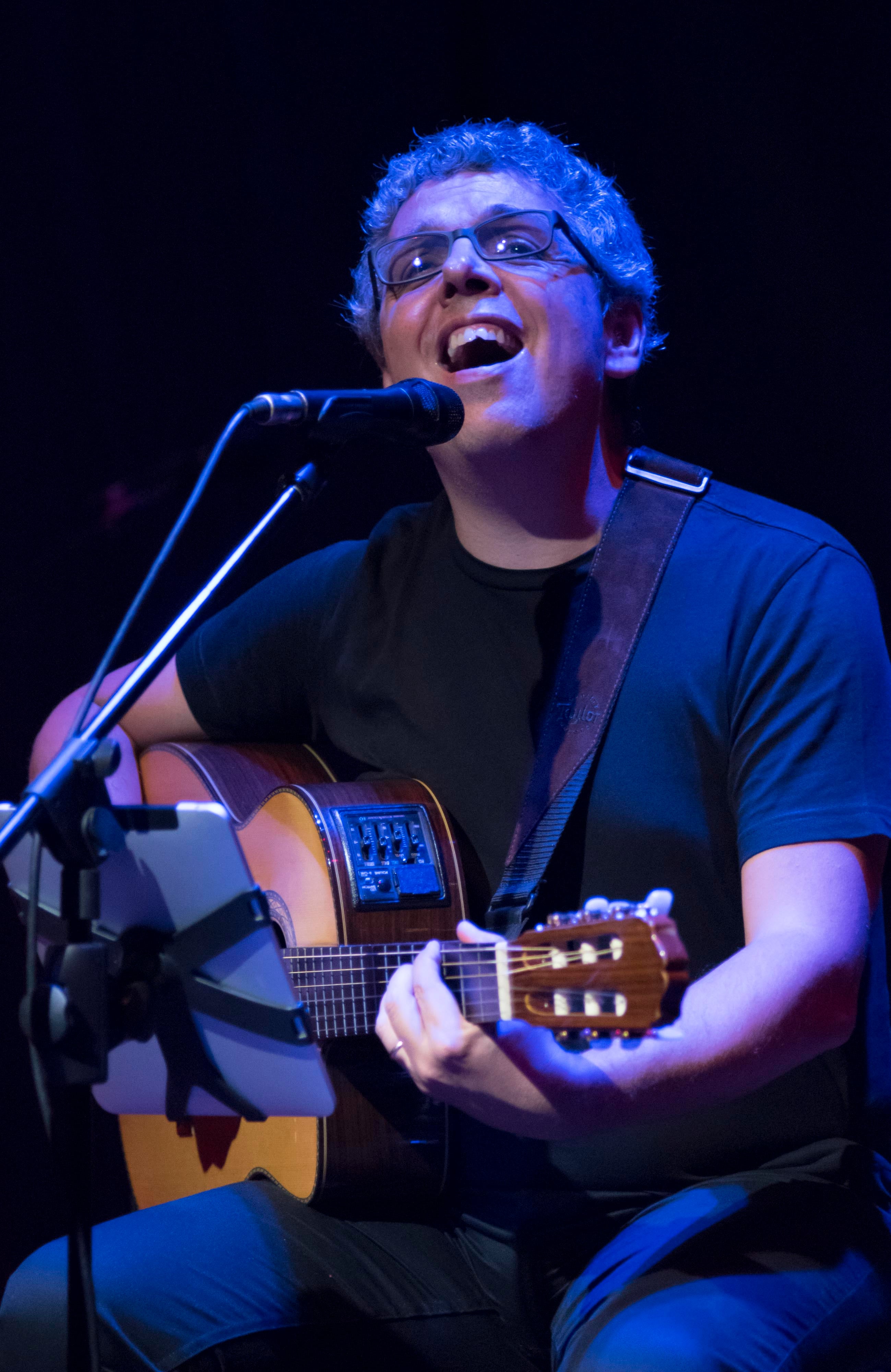 Fotos del cantautor español Pedro Guerra en concierto mientras canta y toca su guitarra.