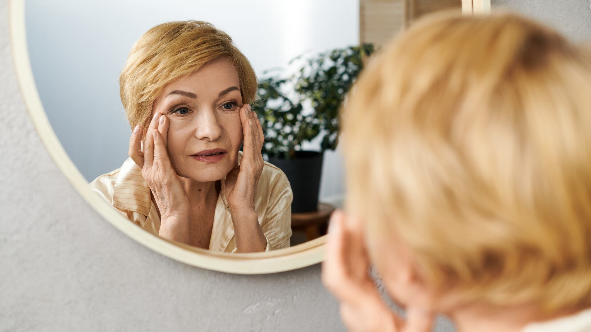 Mujer de edad madura viéndose el rostro al espejo y estirándose las arrugas con los dedos