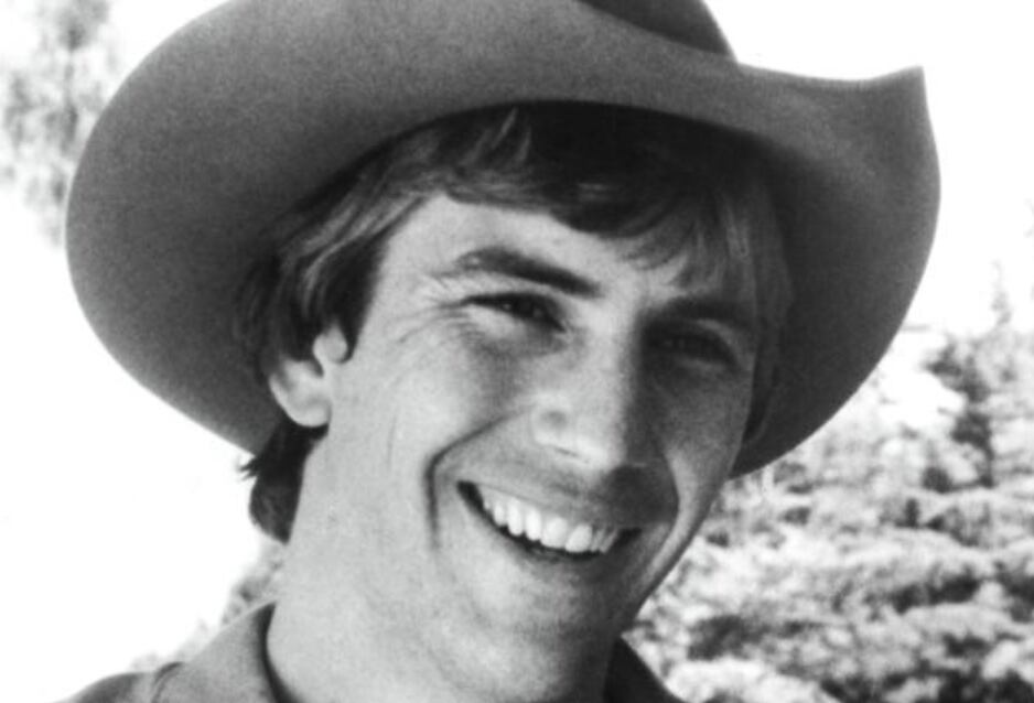 Imagen en primer plano de Kevin Costner en su juventud. Está sonriendo y usa un sombrero vaquero.