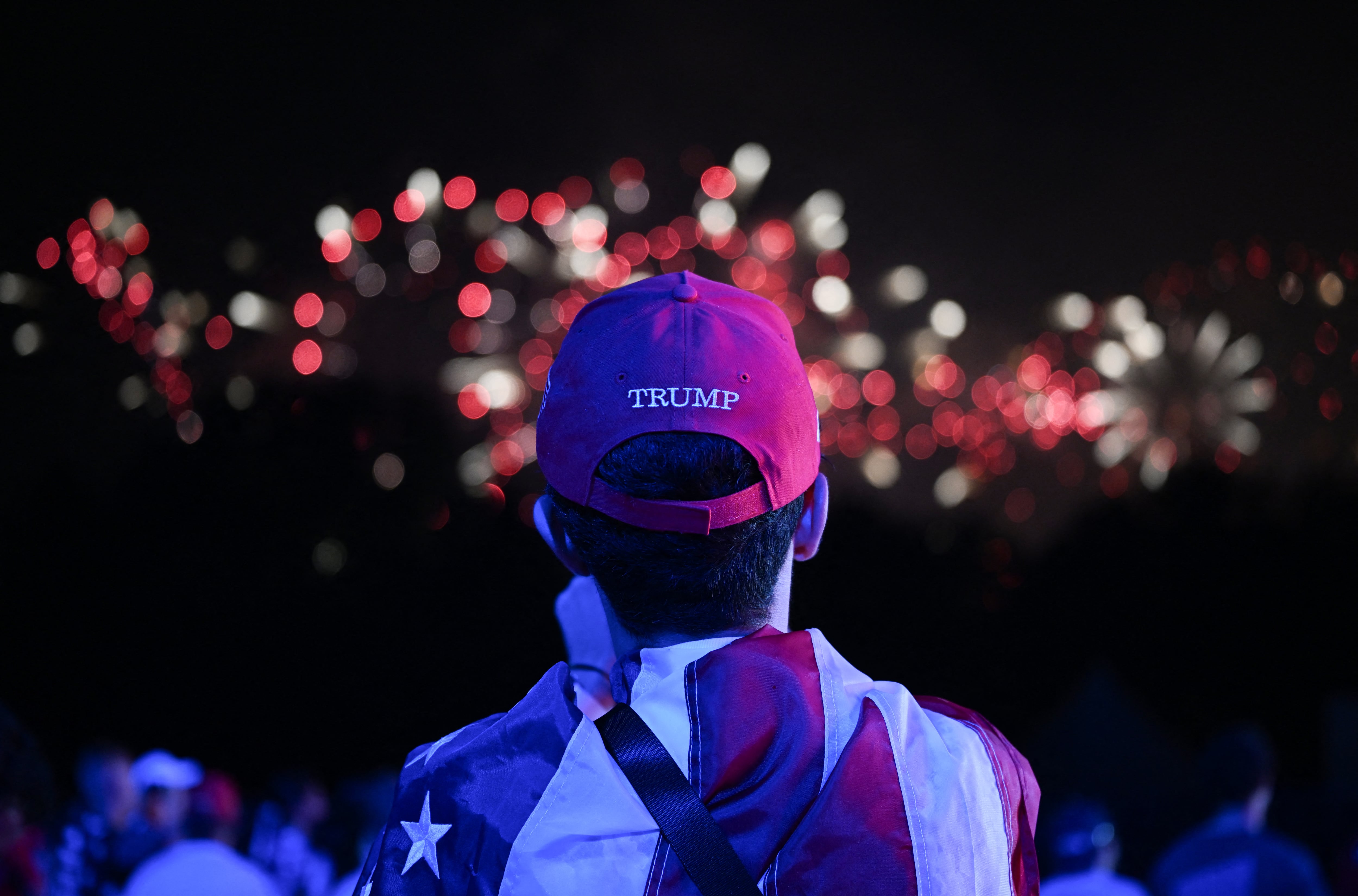 en la imagen alguien con una gorra de Trump y los fuegos artificiales del 4 de julio en el fondo