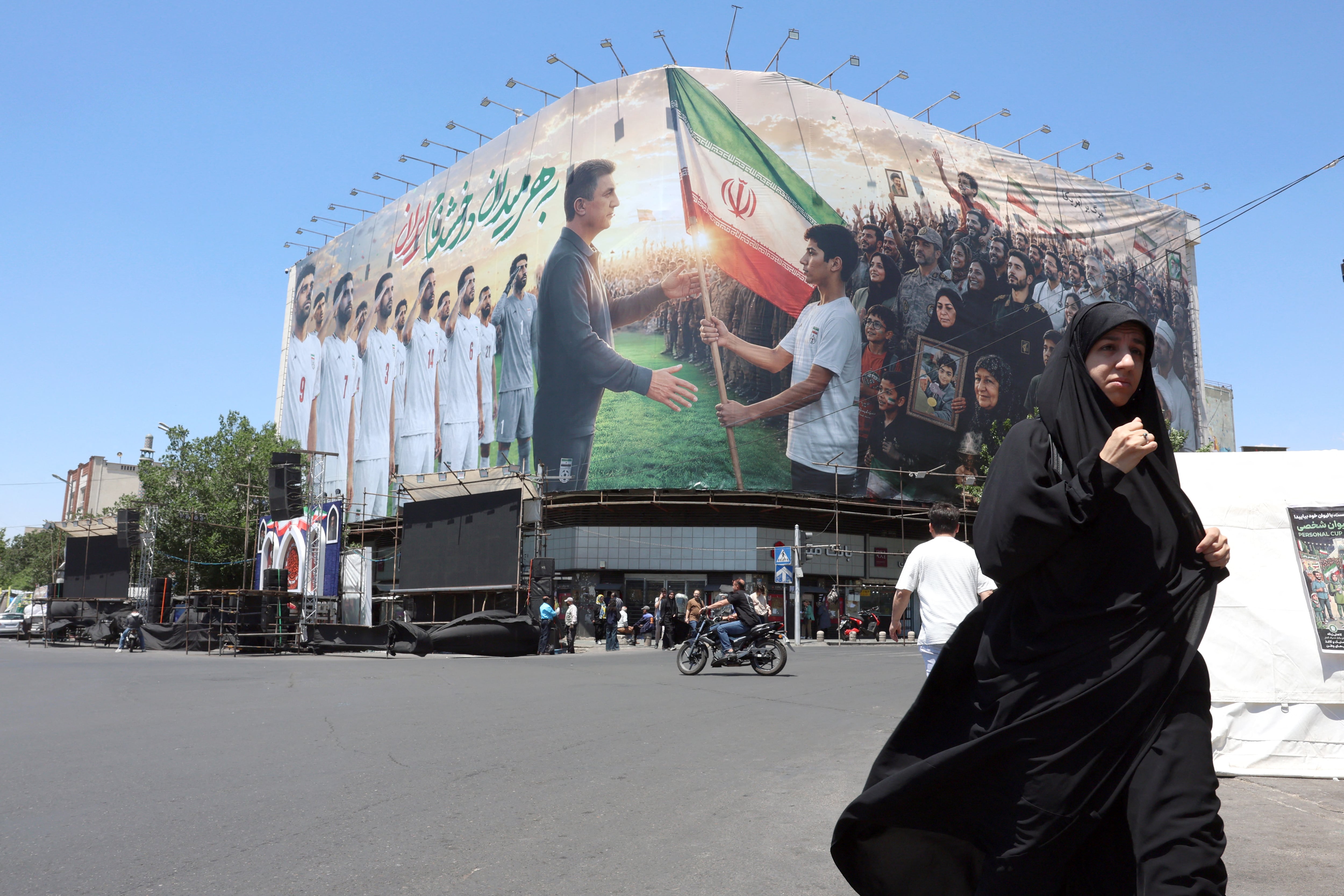 Una mujer iraní camina cerca de un rótulo gigante para apoyar a la Selección de Irán antes del Mundial 2026, en la plaza Enghelab de Teherán.