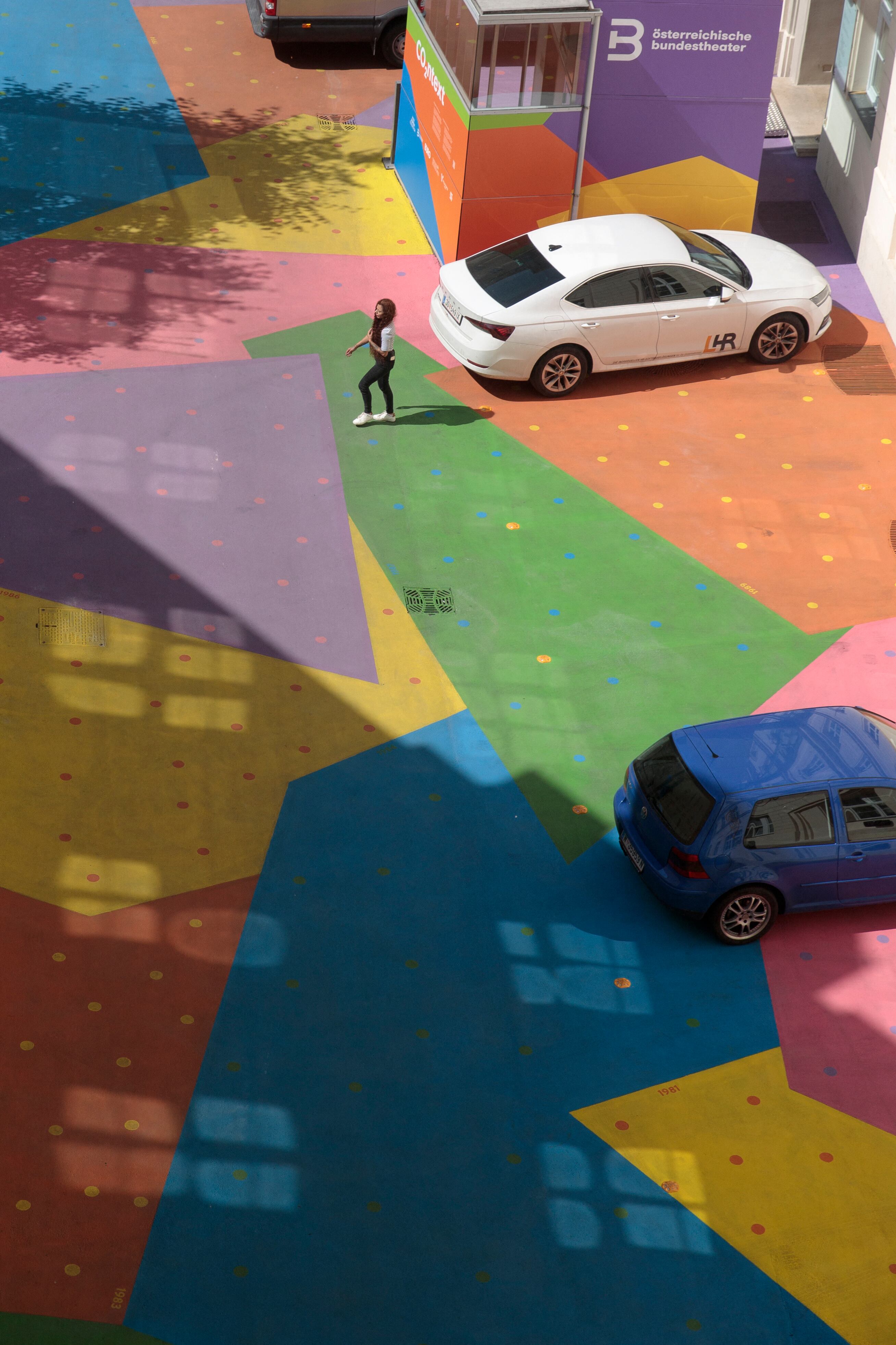 A view from above shows people and cars on the colourfully painted courtyard of the 'Heidi Horten museum' is pictured in Vienna, Austria, on August 13, 2025. To fight extreme heat attributable to climate change, an artist collective has covered the asphalt with reflective paints to lower the temperature, as part of an innovative project in Europe combining art, science, and urban development. (Photo by Alex HALADA / AFP)