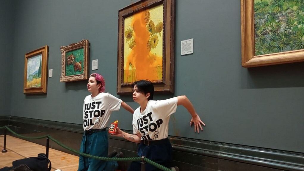 A handout picture from the Just Stop Oil climate campaign group shows activists with their hands glued to the wall under Vincent van Gogh's "Sunflowers" after throwing tomato soup on the painting at the National Gallery in central London on October 14, 2022. - London's Metropolitan Police said its officers arrested two protesters from the Just Stop Oil group for criminal damage and aggravated trespass after they "threw a substance over a painting" at the gallery on Trafalgar Square. (Photo by Handout / Just Stop Oil / AFP) / RESTRICTED TO EDITORIAL USE - MANDATORY CREDIT "AFP PHOTO / JUST STOP OIL " - NO MARKETING - NO ADVERTISING CAMPAIGNS - DISTRIBUTED AS A SERVICE TO CLIENTS