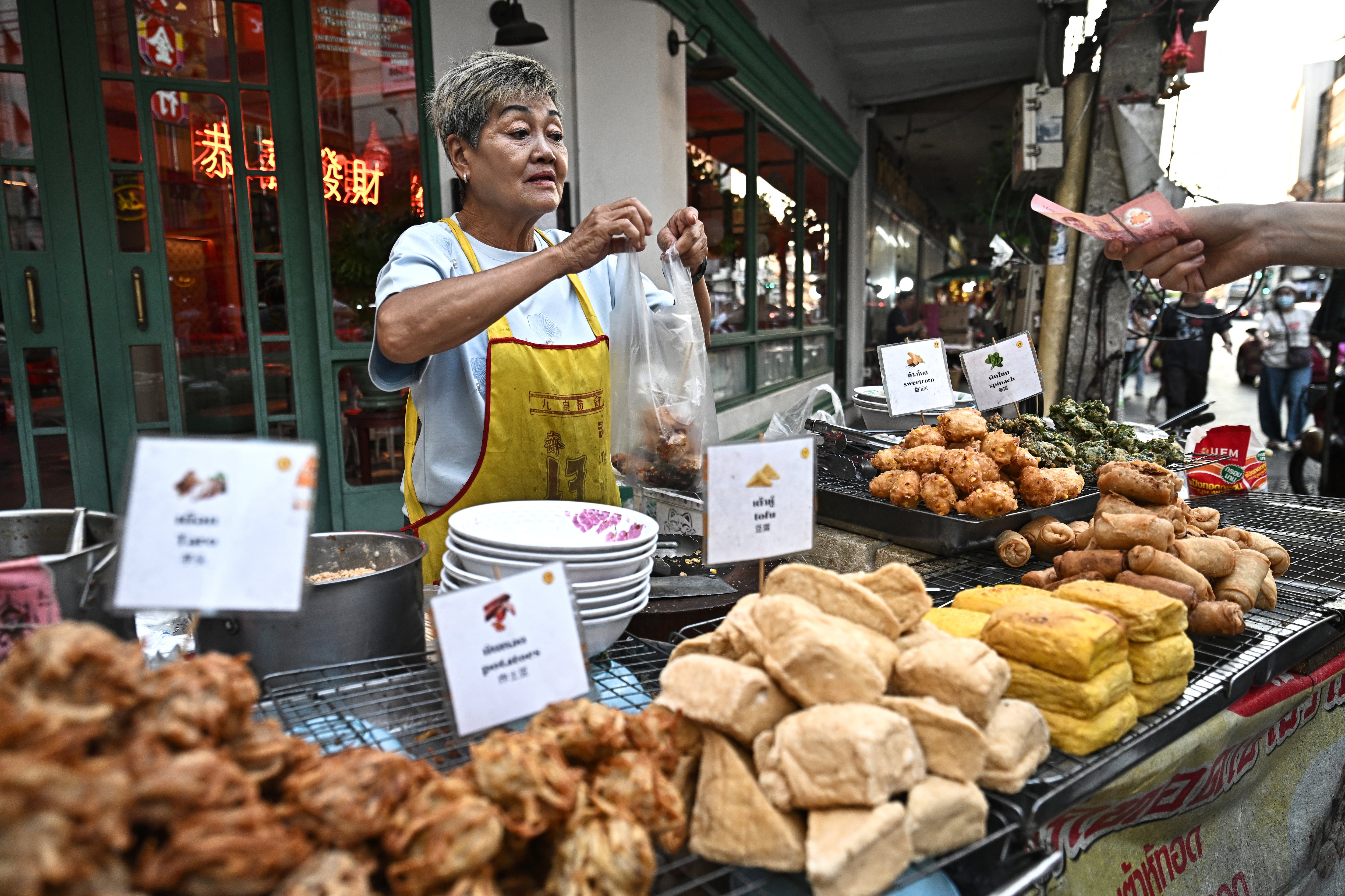 Esta foto, tomada el 29 de abril de 2026, muestra a la vendedora ambulante de comida Thitisakulthip Sang‑uamsap vendiendo bocadillos vegetarianos fritos en el barrio chino de Bangkok.