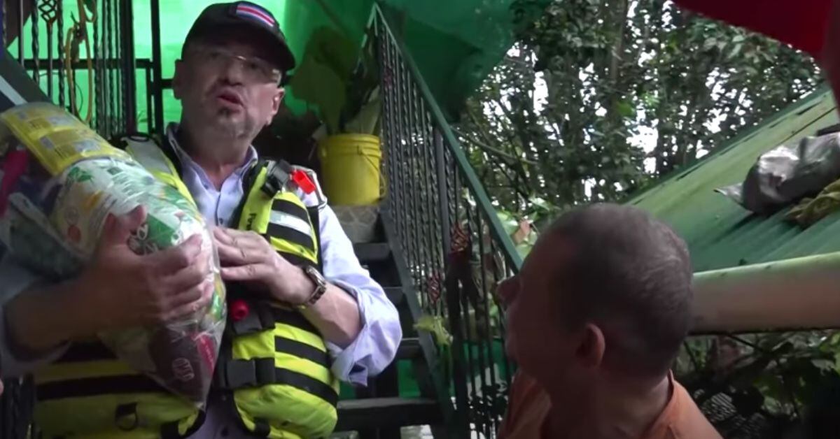 Rodrigo Chaves sostiene un paquete de alimentos donados por El Salvador mientras conversa con un damnificado por lluvias en Guanacaste, mencionando críticas infundadas de diputados sobre el uso de las donaciones.