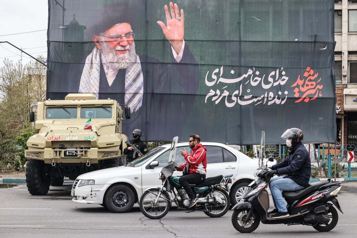 Viajeros pasan junto a un vehículo de las fuerzas de seguridad iraníes estacionado bajo una pancarta en honor al líder supremo iraní fallecido, el ayatolá Ali Khamenei, en Teherán el 31 de marzo de 2026.