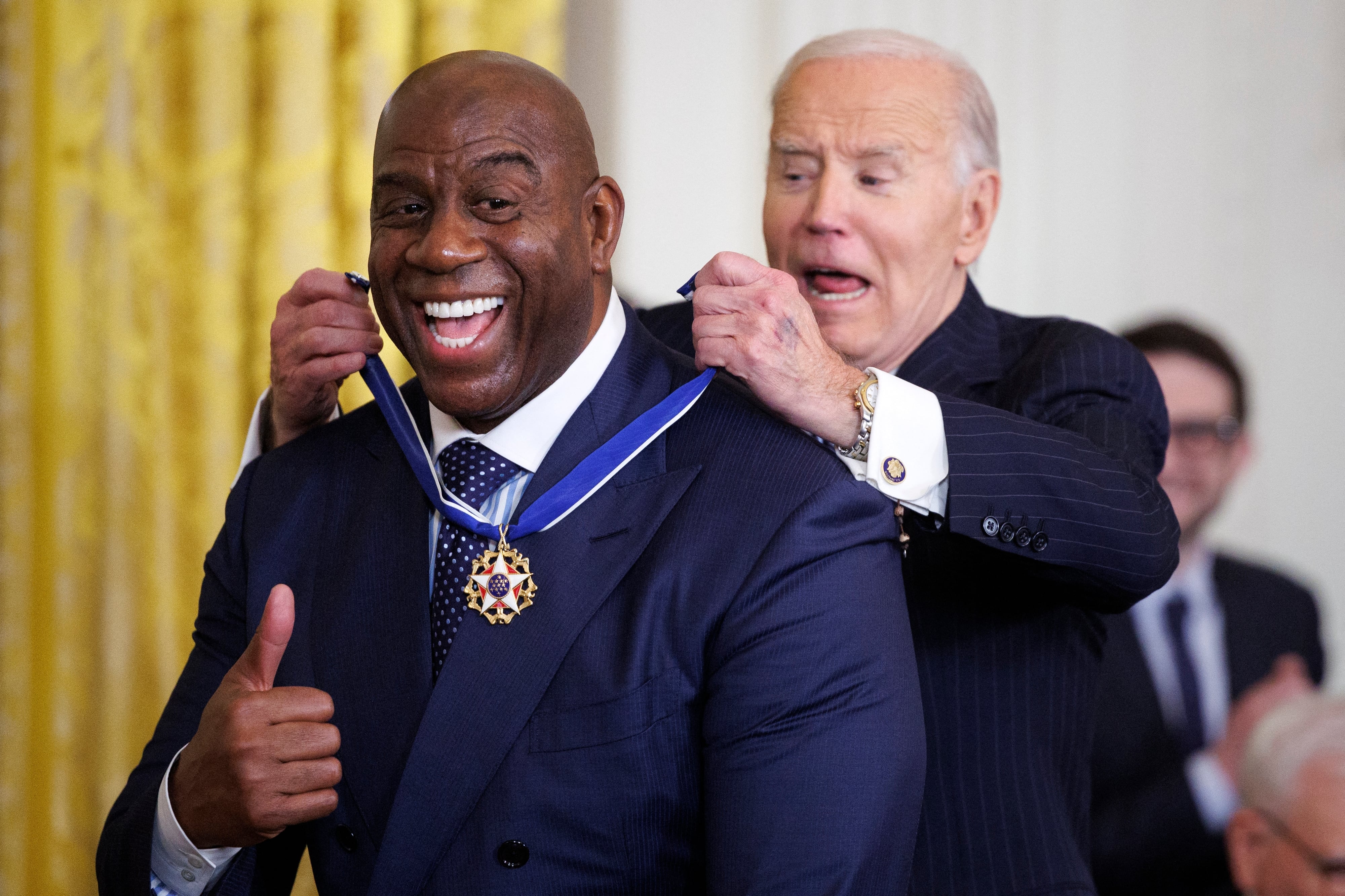 Magic Johnson sonriendo y alzando un dedo en señal de aprobación mientras el presidente Joe Biden le coloca la Medalla de la Libertad.