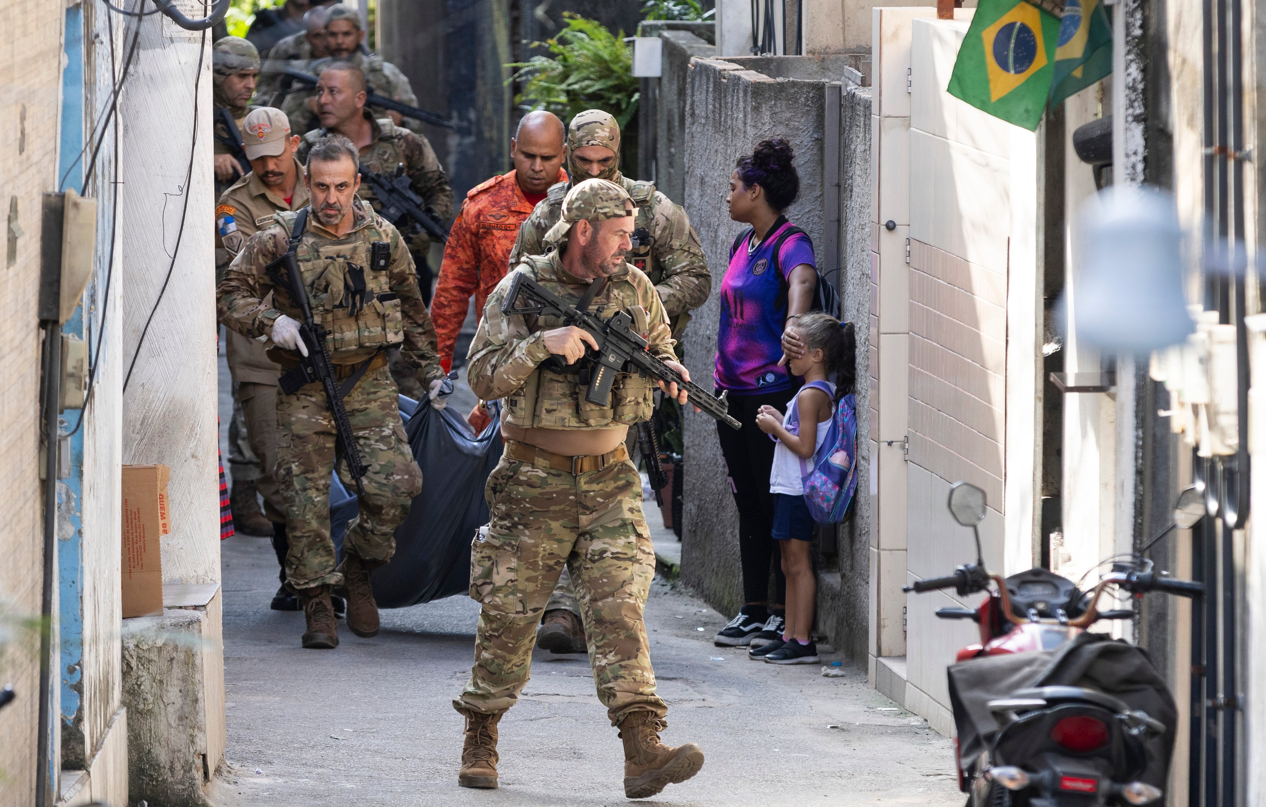 "Antes de que ella vea". Pie de foto: Una mujer cubre el rostro de un niño mientras la policía pasa con el cuerpo de un sospechoso asesinado en un operativo en Ladeira dos Tabajaras. La imagen fue elegida porque simboliza la violencia urbana en Río de Janeiro y es una de las imágenes más premiadas del año por el periódico O Globo.