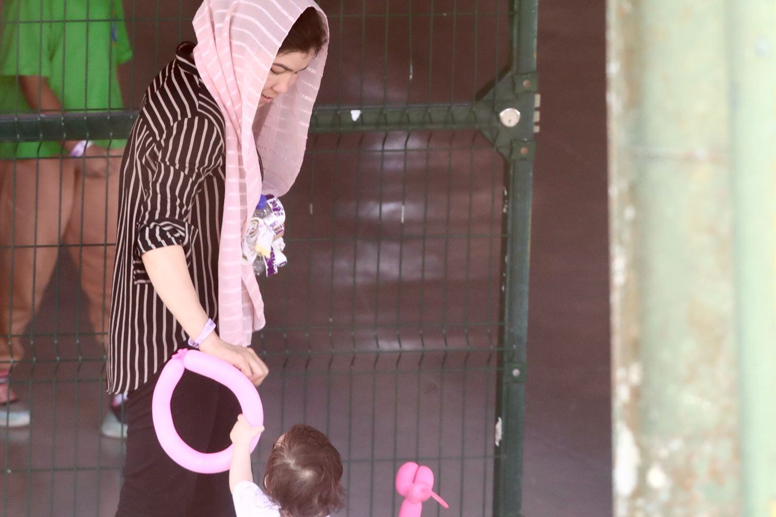 Mujer lleva a una niña de la mano, quien tiene un globo rosado, en el albergue CATEM en la zona sur.