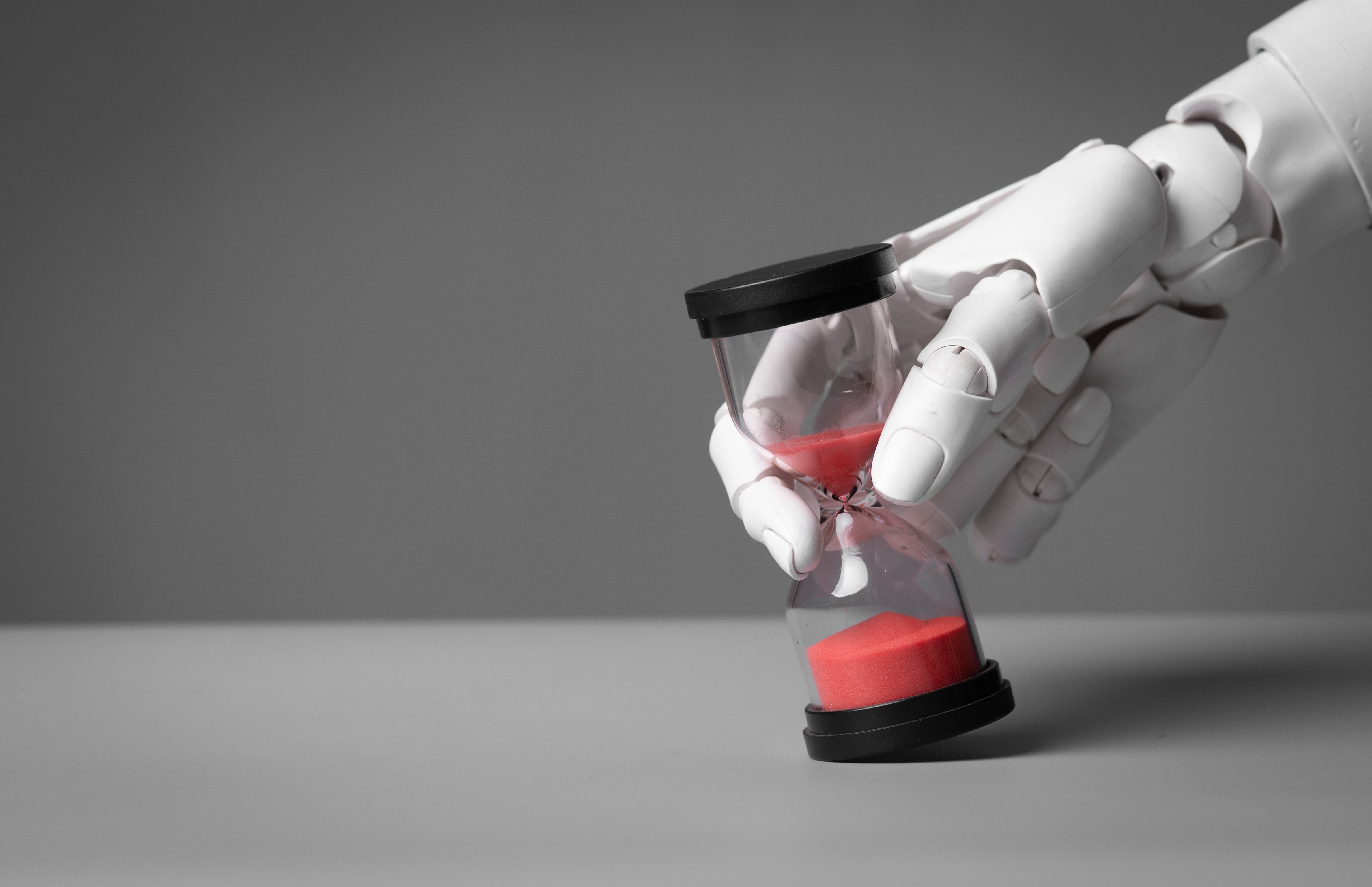 Dedo de robot humanoide sostiene reloj de arena. El tiempo corre y se acaba para fijar limitaciones a la inteligencia artificial (IA)