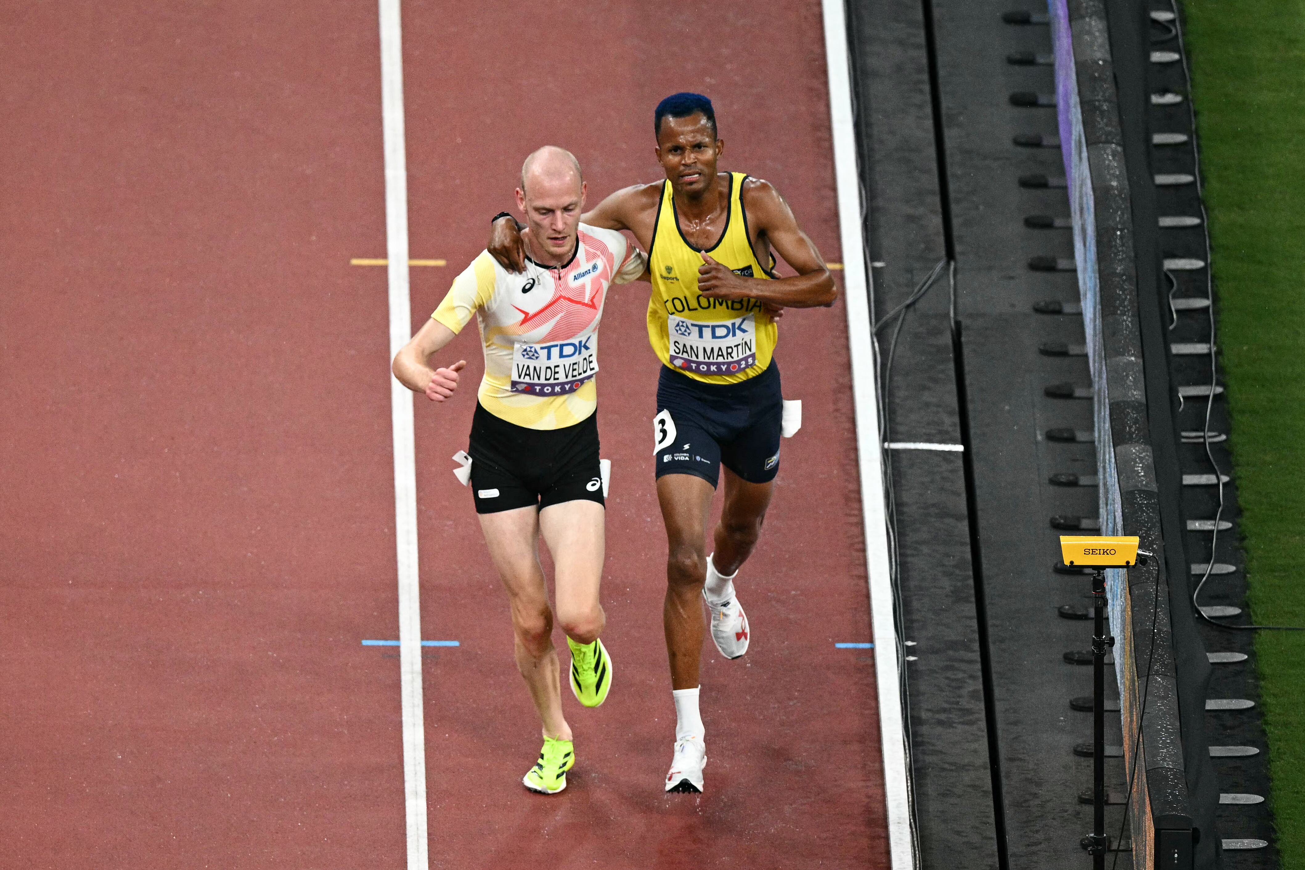 Belgium's athlete Tim Van De Velde (L) helps Colombia's Carlos San Martin as they compete in the men's 3000m steeplechase heats during the World Athletics Championships in Tokyo on September 13, 2025. (Photo by Philip FONG / AFP)