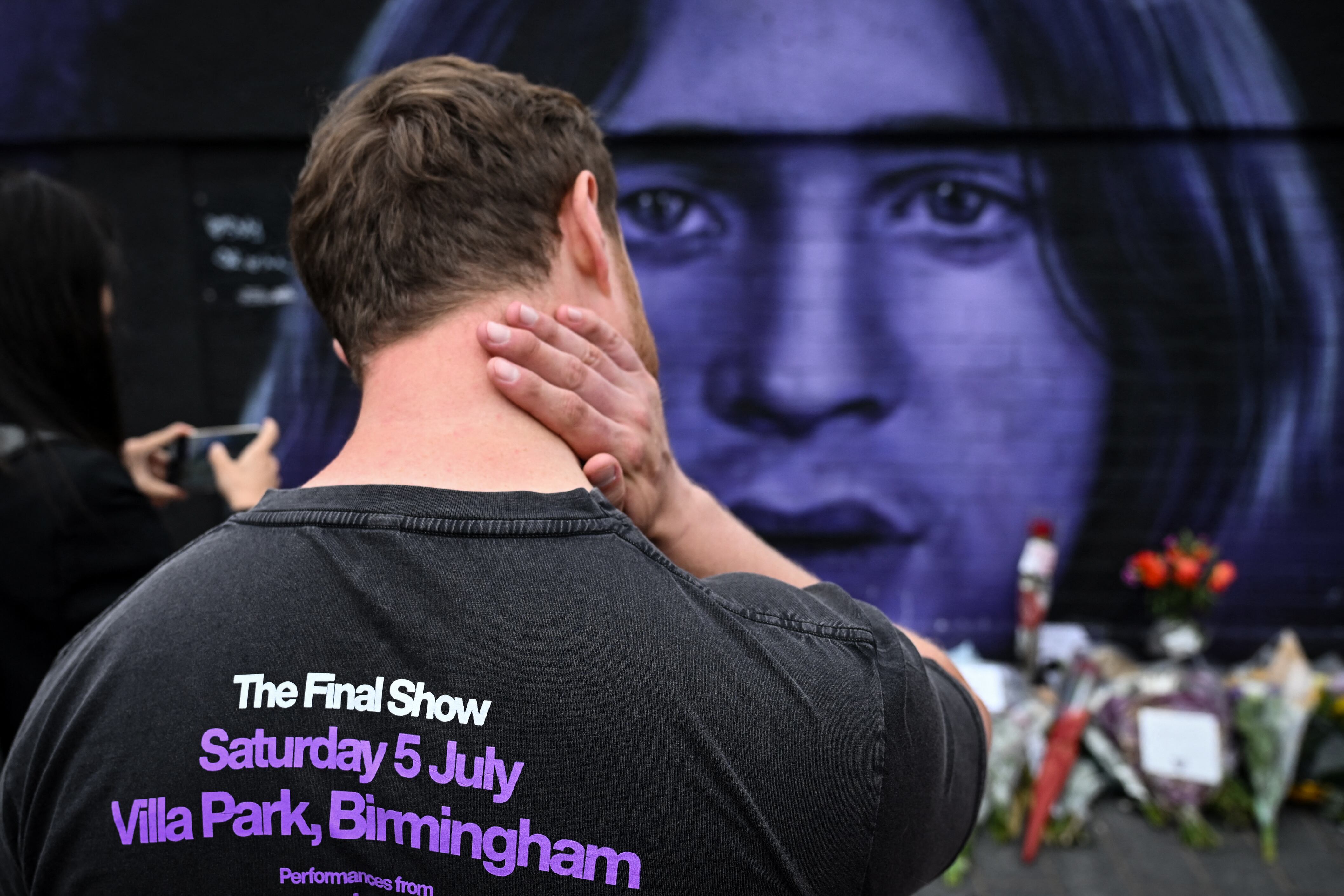 Fans gather around a makeshift memorial by a mural depicting late British singer-songwriter Ozzy Osbourne as they pay a tribute to late artist, in Birmingham, central England, on July 23, 2025 a day after his death. Tributes poured in on July 23, 2025 for hell-raiser singer Ozzy Osbourne as tearful fans laid flowers in his hometown and his Black Sabbath band mates mourned the death of their legendary heavy metal frontman, just weeks after he played an epic farewell concert in their Birmingham hometown. Osbourne, nicknamed the "Prince of Darkness" who famously once bit off the head of a bat while on stage, died on July 22, 2025 at the age of 76, his family said. (Photo by JUSTIN TALLIS / AFP)