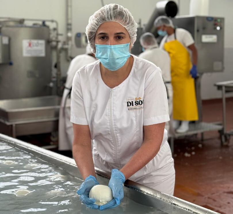 Una mujer sostiene queso mozarrella elaborado de leche de búfala durante su proceso en una planta de producción. Ella está vestida con indumentaria para manipular alimentos.