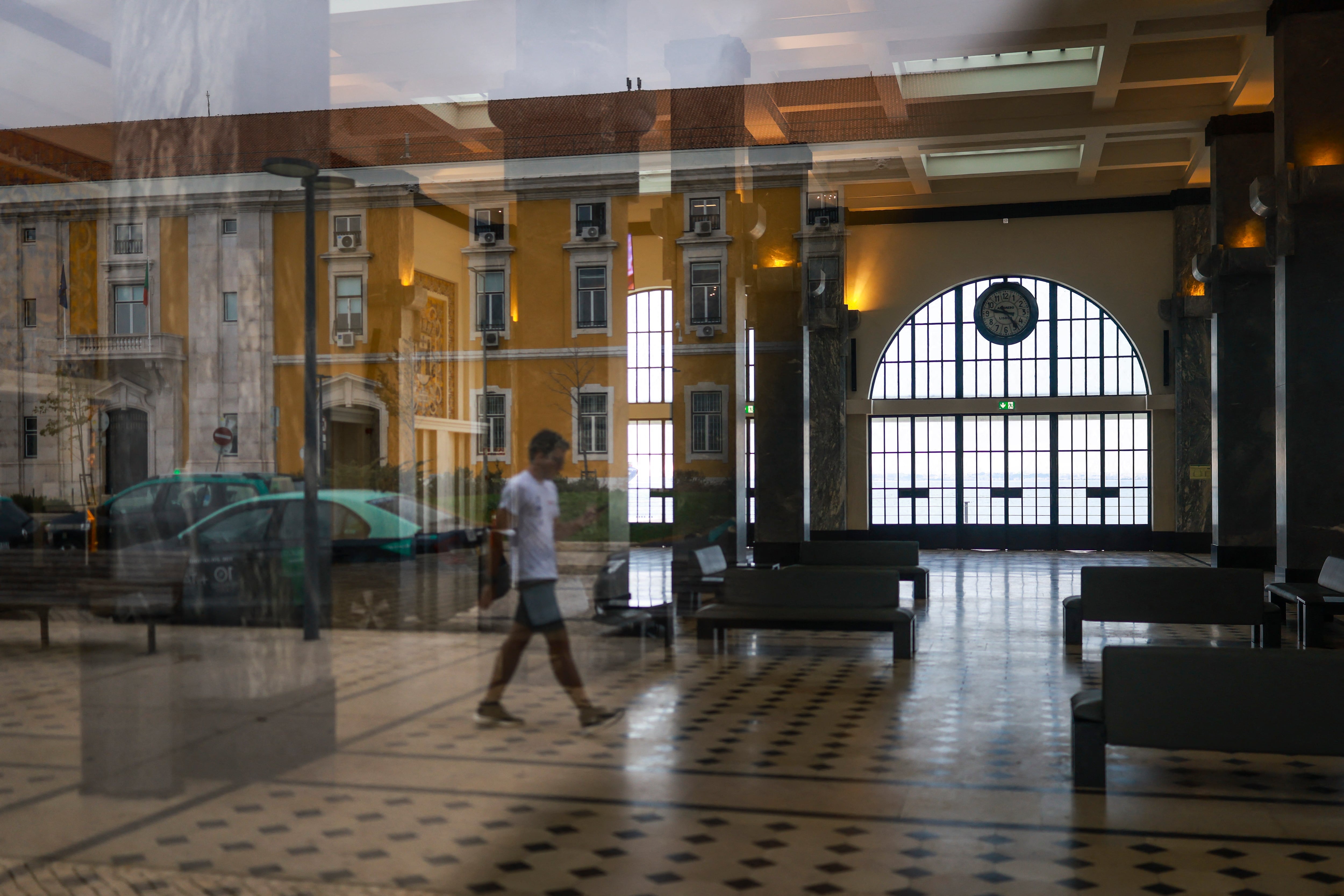 Un peatón se refleja en la ventana de una estación de barcos vacía de Terreiro do Paco, cerrada durante una huelga general en Lisboa este 11 de diciembre. Fotografía: