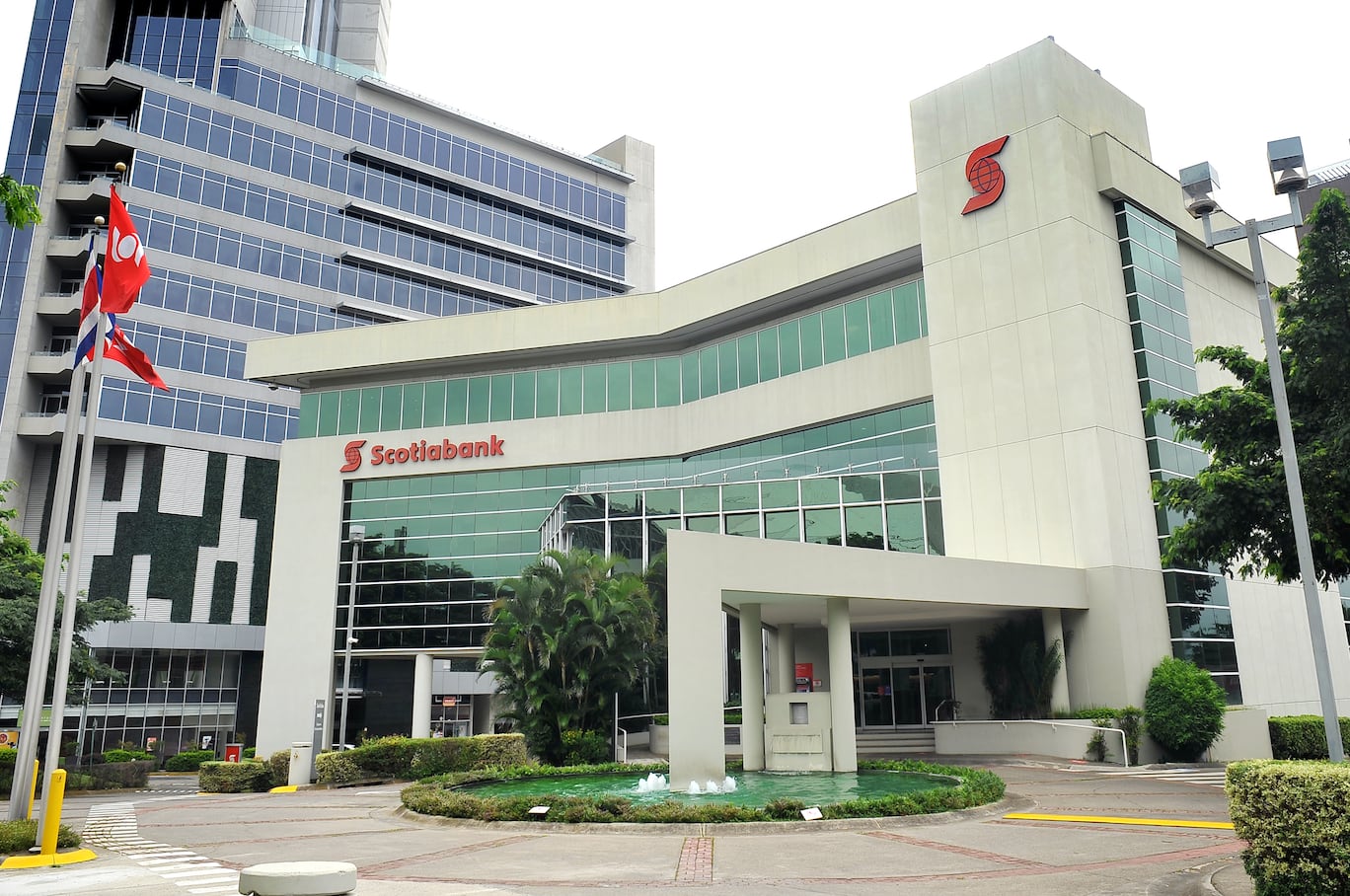 Fachada del edificio principal de Scotiabank en Costa Rica, con la bandera nacional ondeando al frente, en el contexto del anuncio de un acuerdo de absorción por parte de Banco Davivienda.