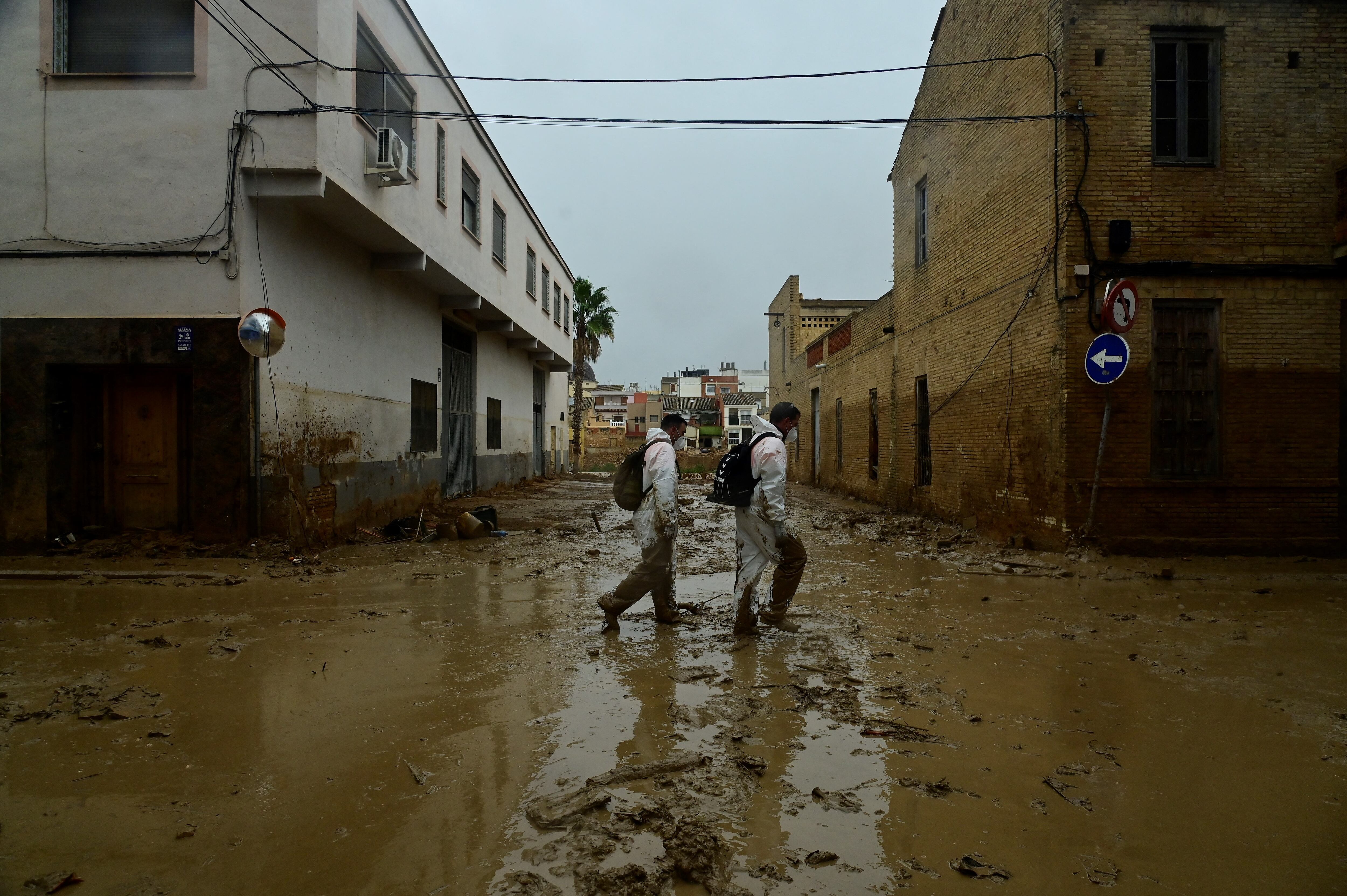 Hombres con trajes de protección caminan por una calle cubierta de barro en Paiporta, al sur de Valencia, en el este de España.