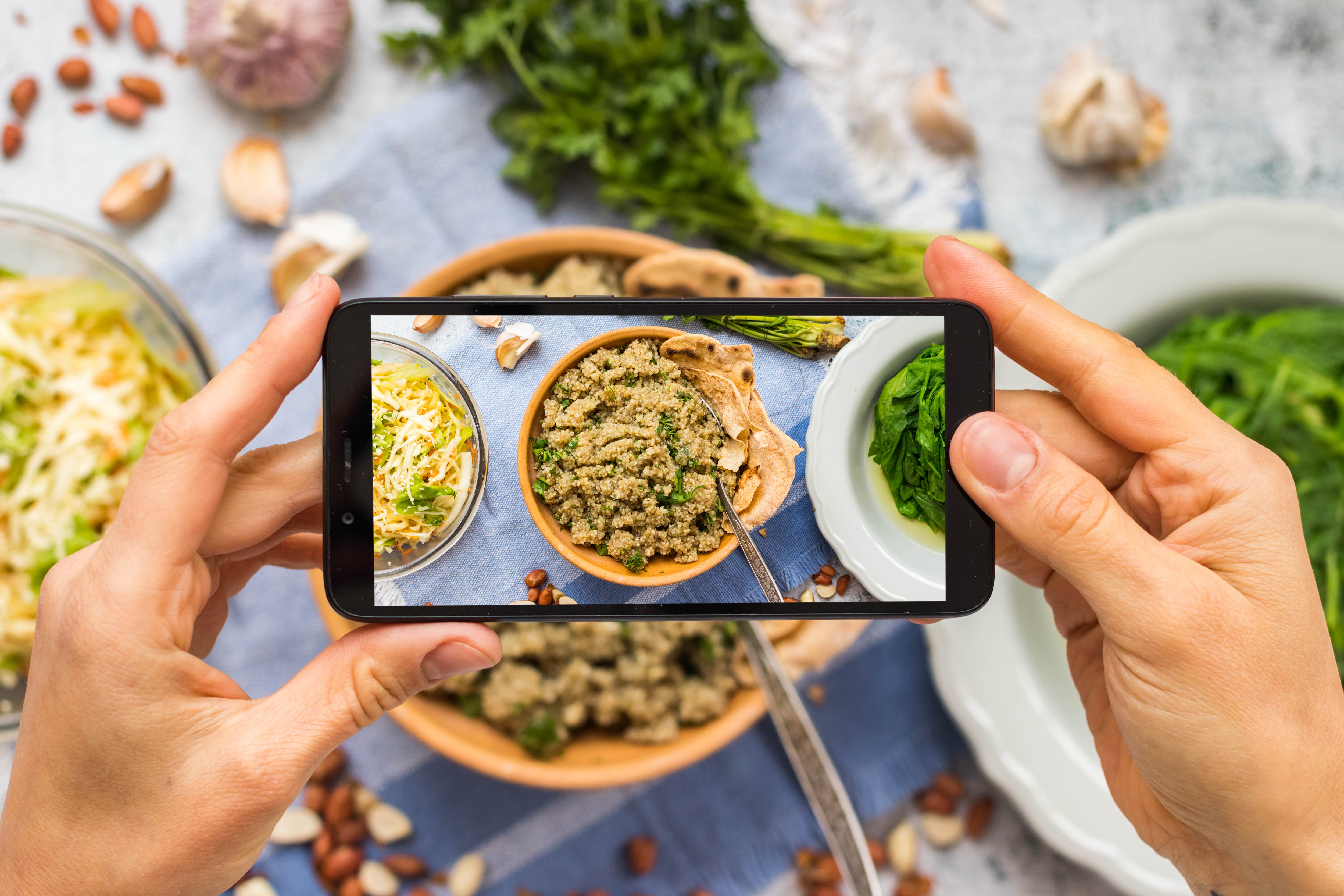 Fotos de platillos para subir a redes sociales. Plano detalle de manos sujetando un teléfono que capta imágenes de alimentos, platos, ensaladas