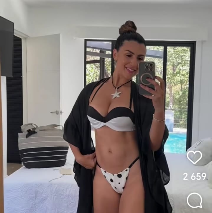 Nicole Aldana usando un traje de baño blanco y negro y una salida de playa de color negro.