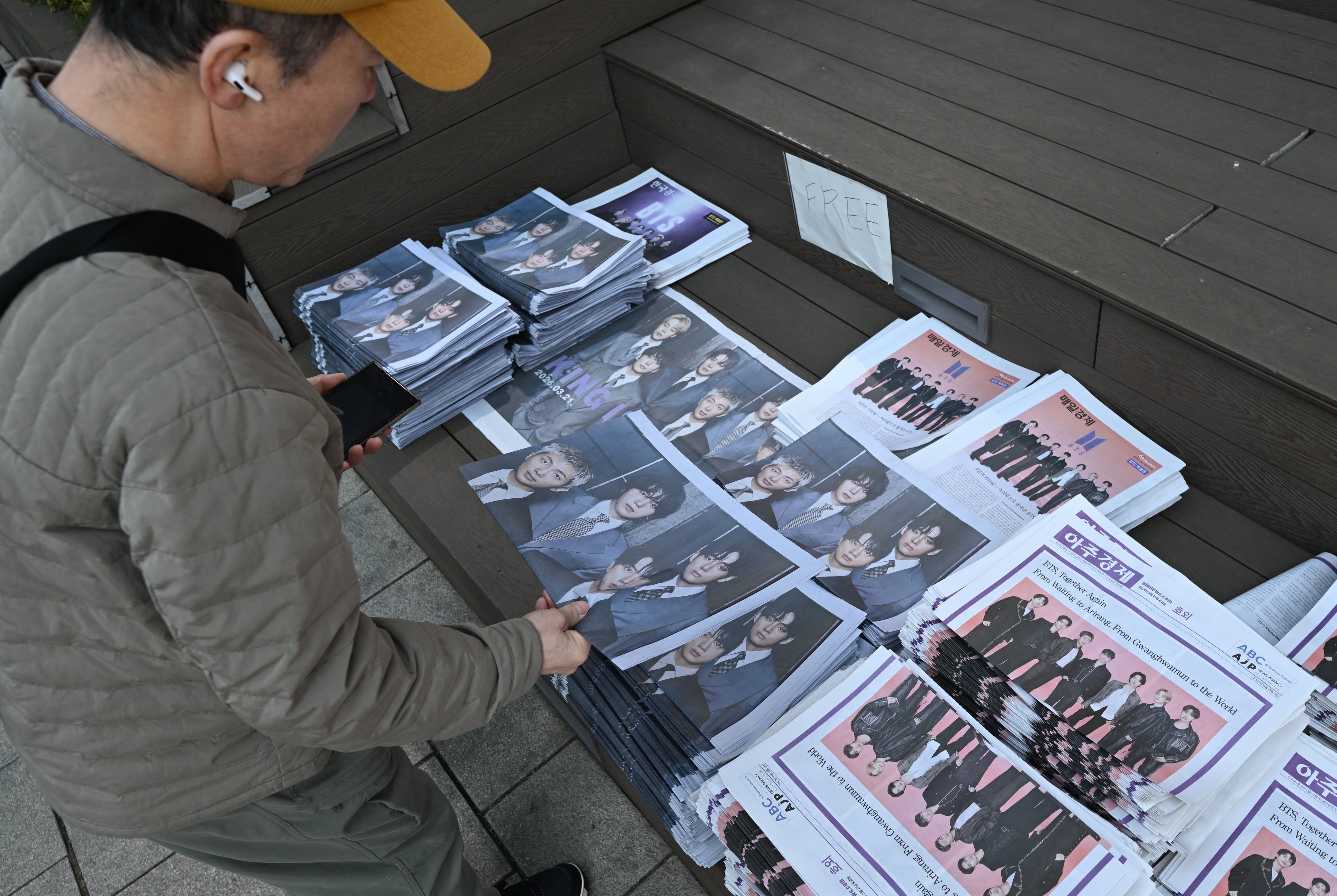 Un hombre recoge ediciones extra de periódicos que informan sobre el regreso de BTS cerca del recinto del concierto de regreso del grupo de K-pop BTS, en el centro de Seúl, el 21 de marzo de 2026.