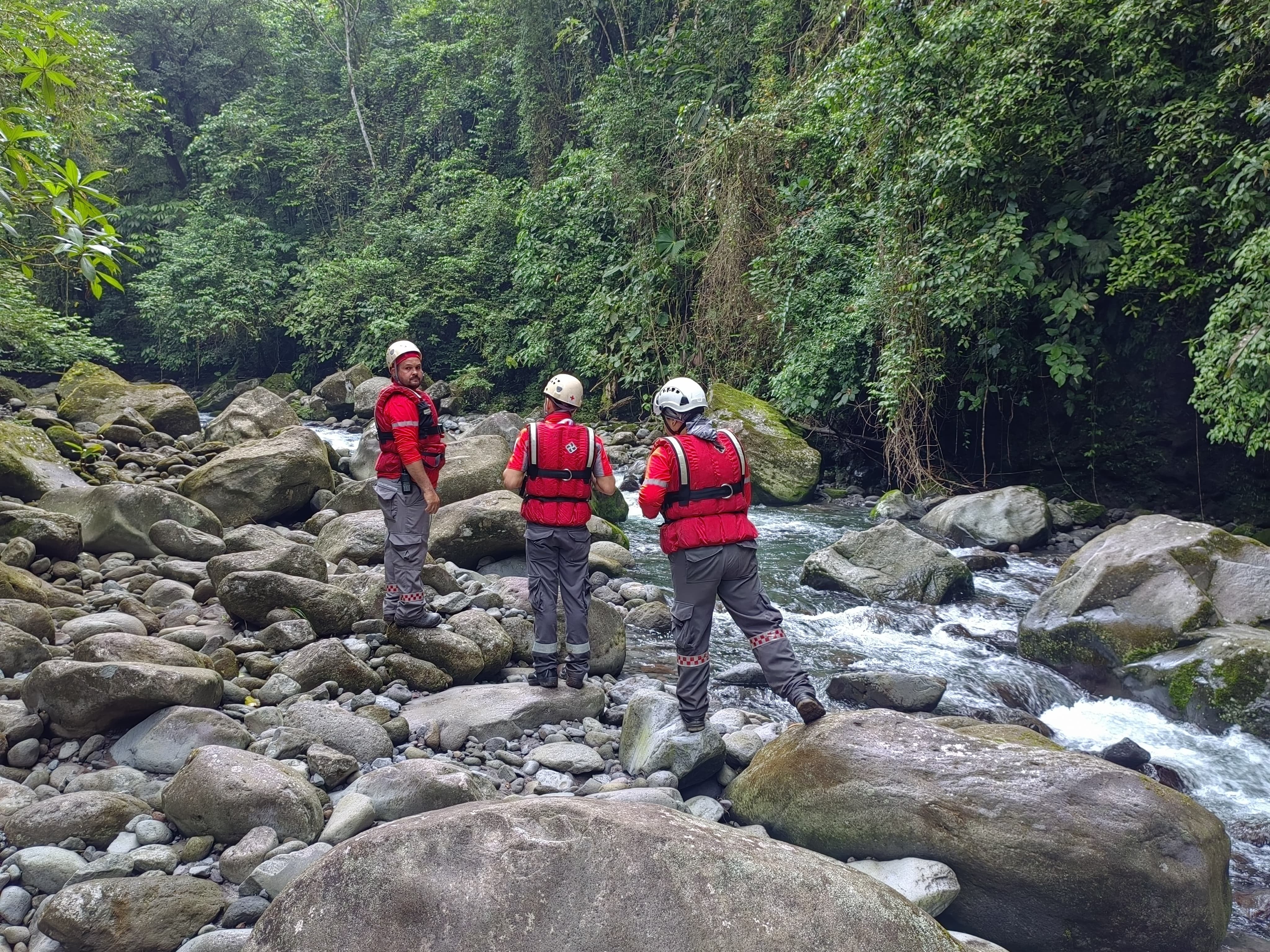Tres cruzrojistas en un río en un bosque realizando labores de rescate.