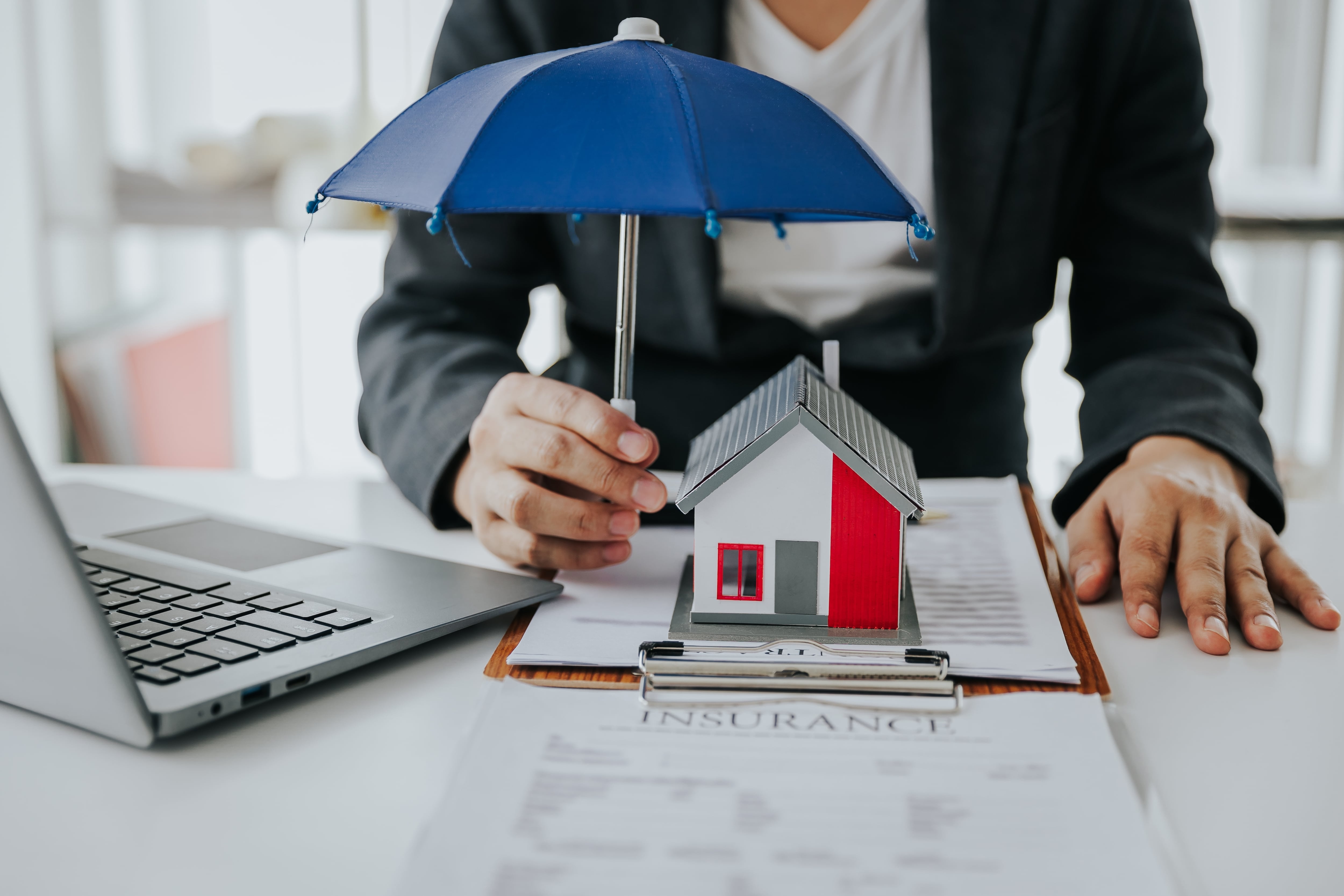 En la imagen alguien sosteniendo un paraguas sobre unas figuras a escala de una casa y personas